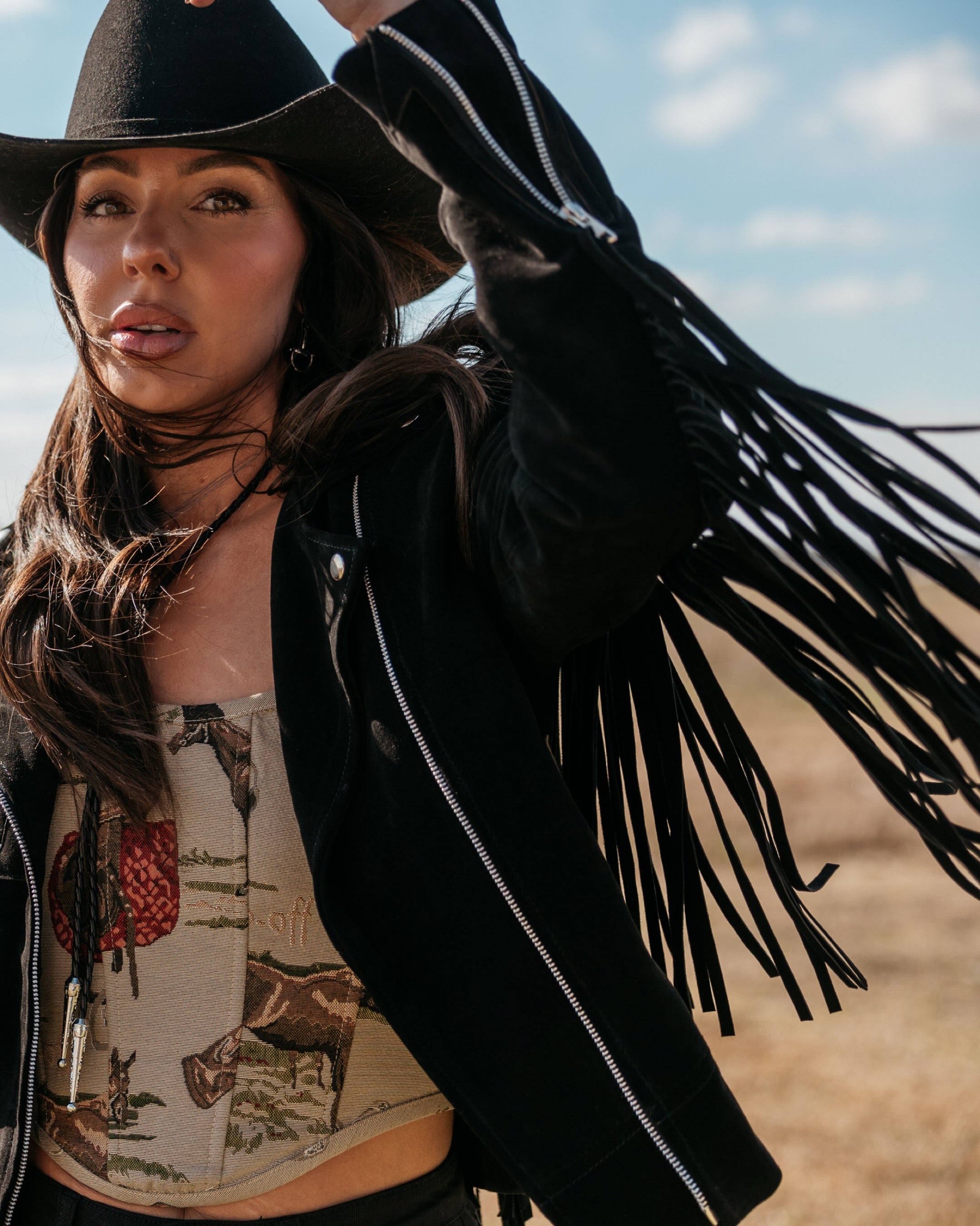 Woman in black cowboy hat and fringe suede jacket, western boho outfit outdoors