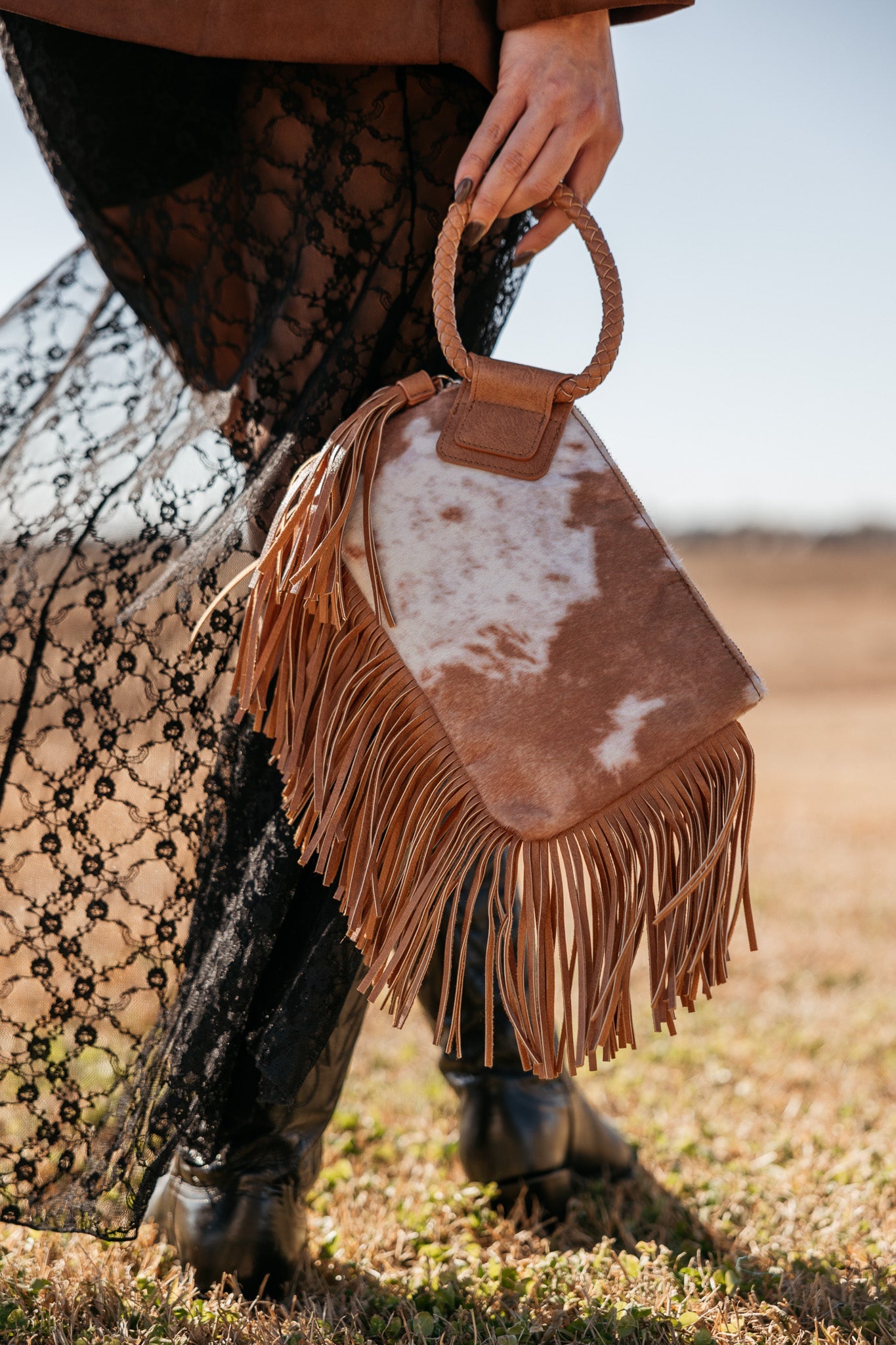 Cow print fringe handbag with braided handle, styled with black lace skirt and western boots
