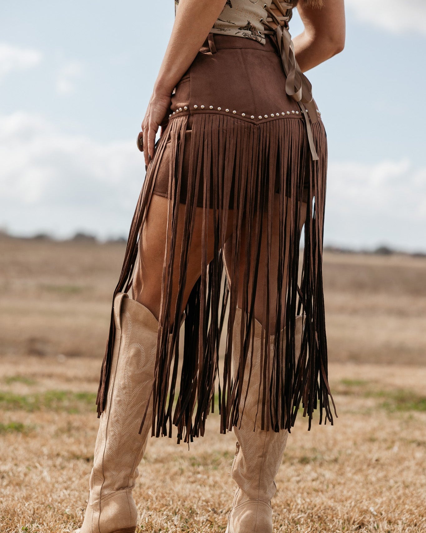Woman wearing brown fringe western skirt with stud details and cowboy boots outdoors