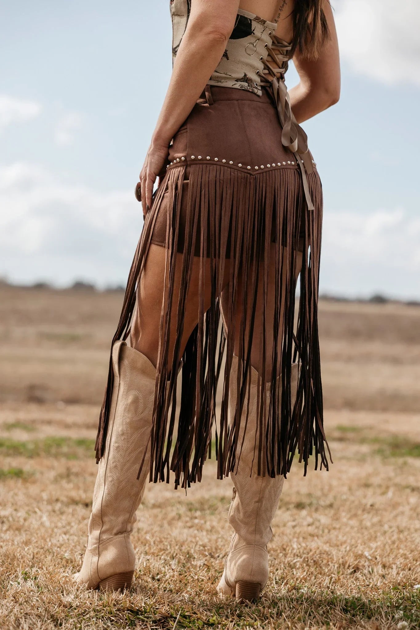 Woman wearing brown fringe western skirt with stud details and cowboy boots outdoors