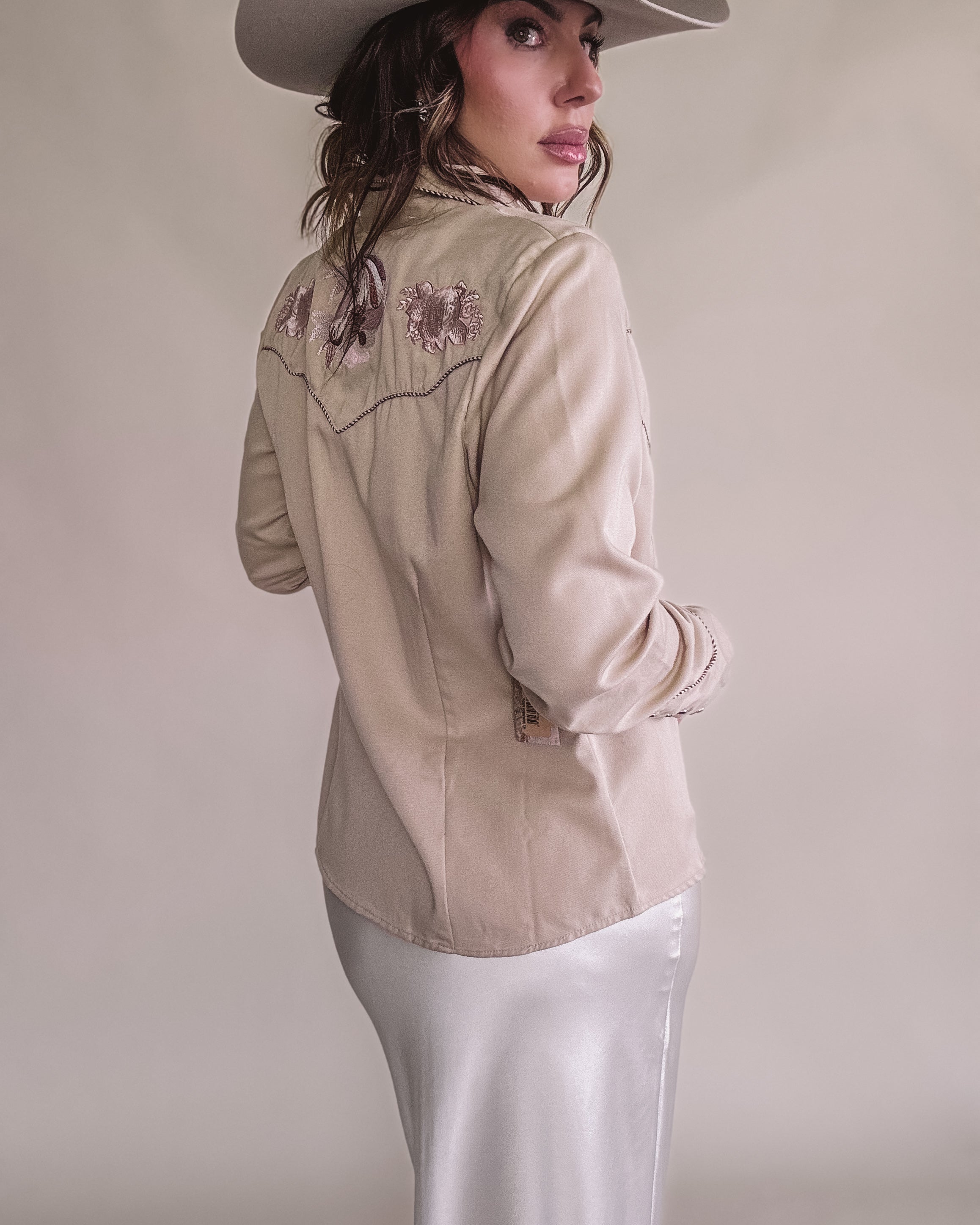 Woman in cream western embroidered shirt, satin skirt, and cowboy hat, western boho style