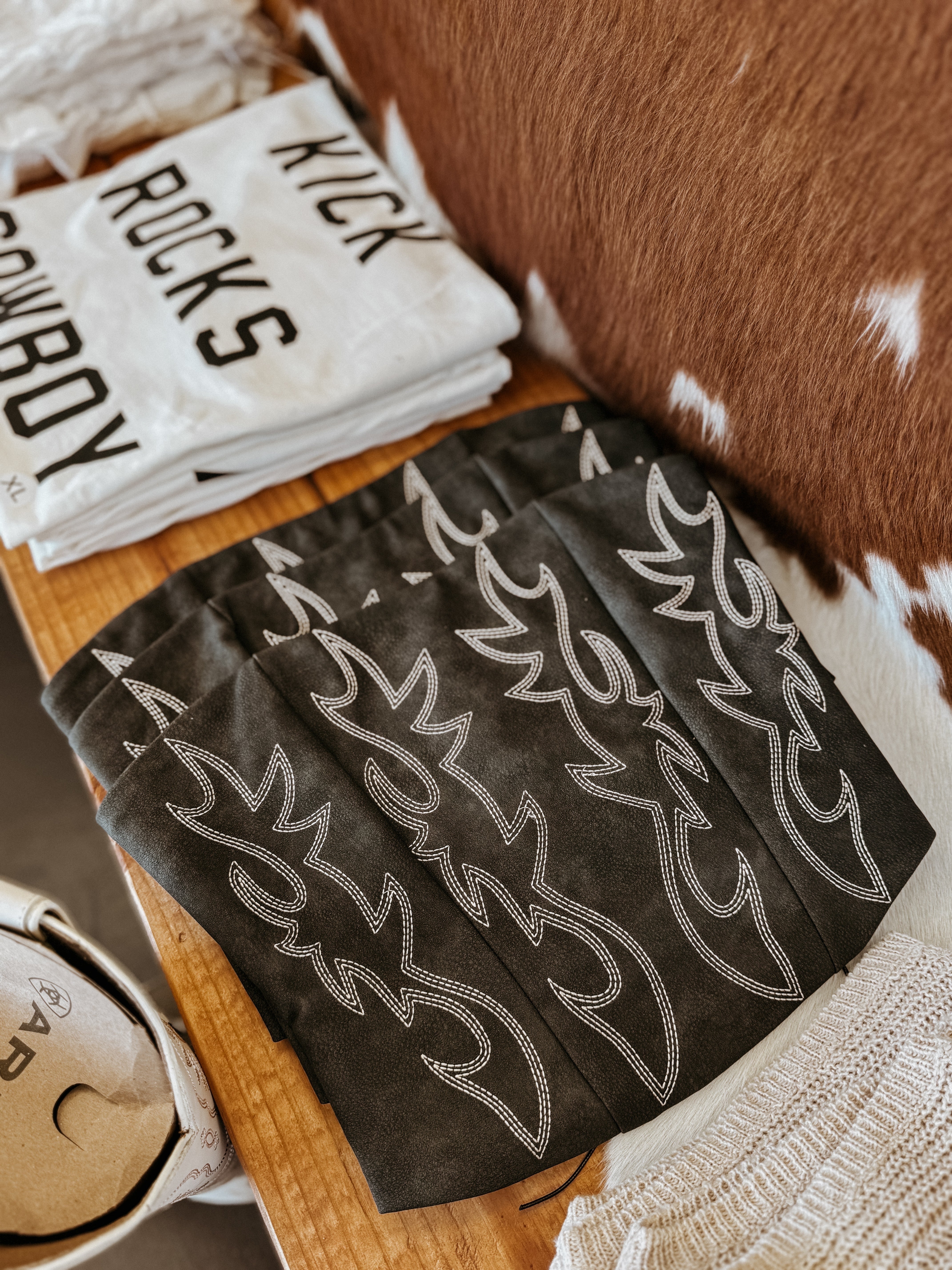 Western-themed graphic tees and embroidered cowgirl accessories on a wooden display