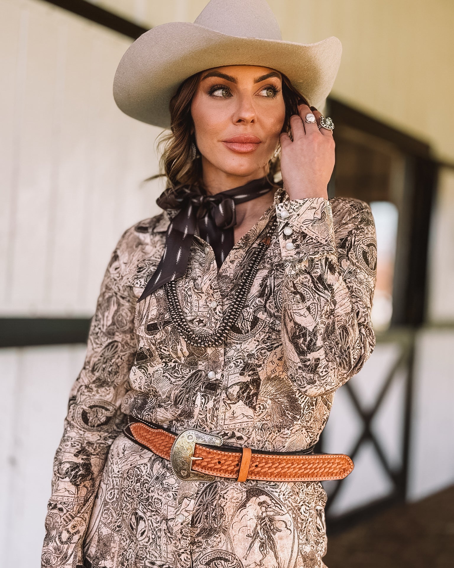 Woman in a beige cowboy hat, western print dress, concho belt, and scarf, western style outfit