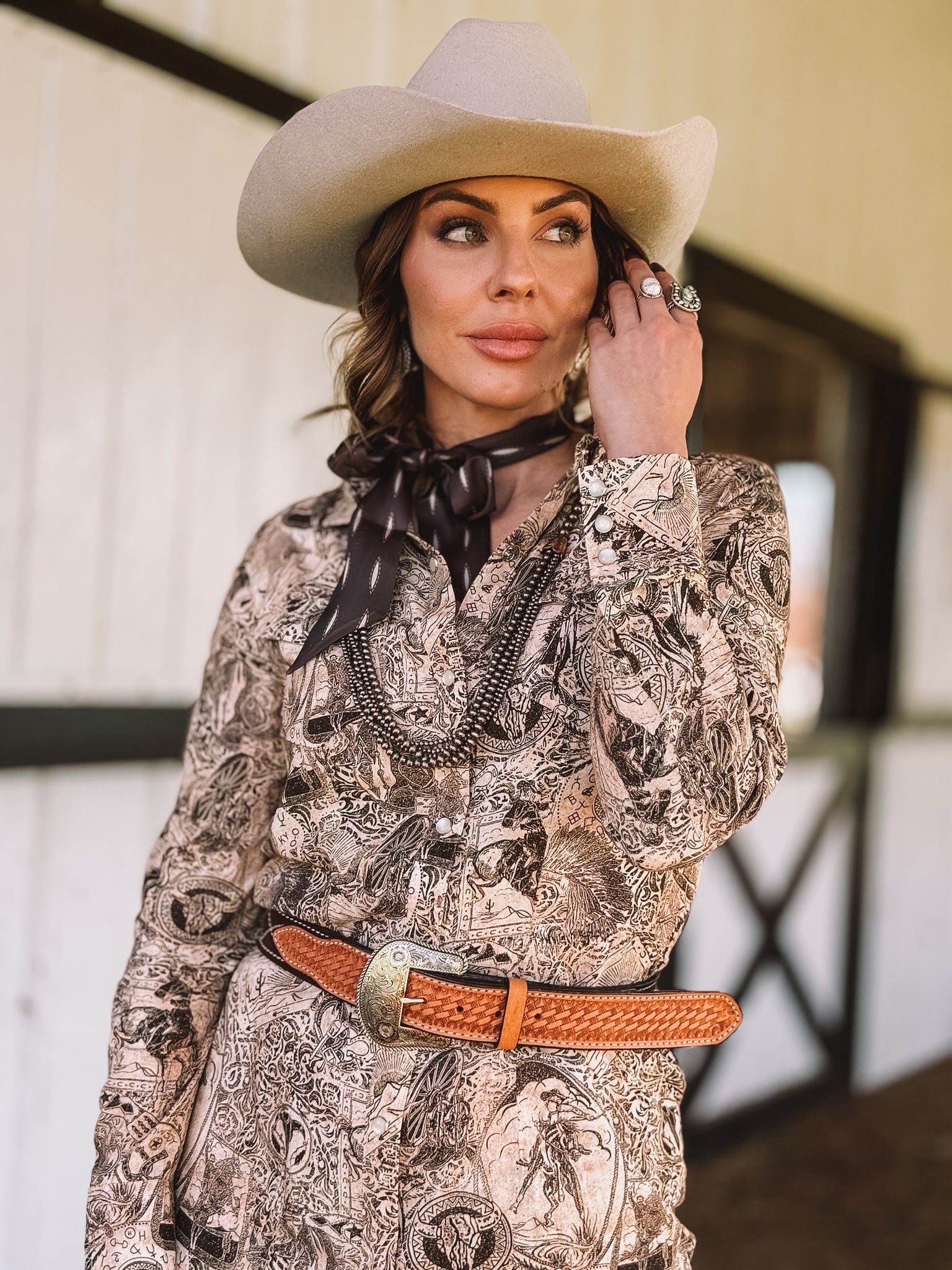 Woman in a beige cowboy hat, western print dress, concho belt, and scarf, western style outfit