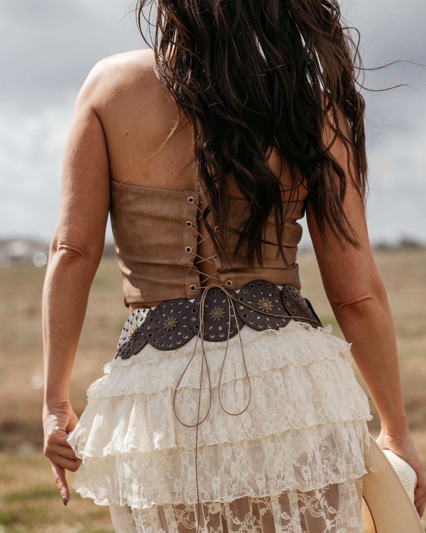 Woman in boho western lace skirt, leather corset top, and concho belt outdoors