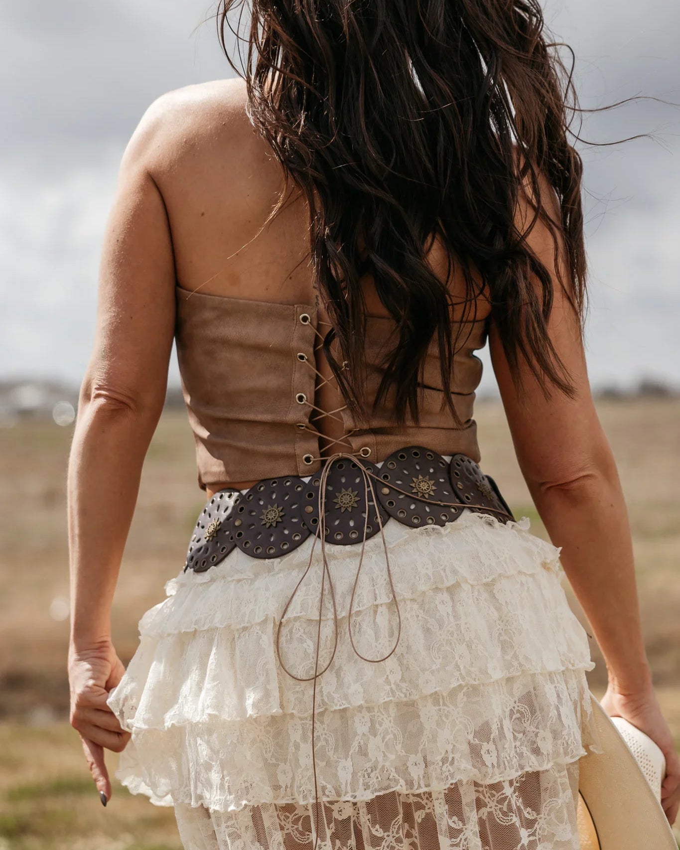Woman in boho western lace skirt, leather corset top, and concho belt outdoors
