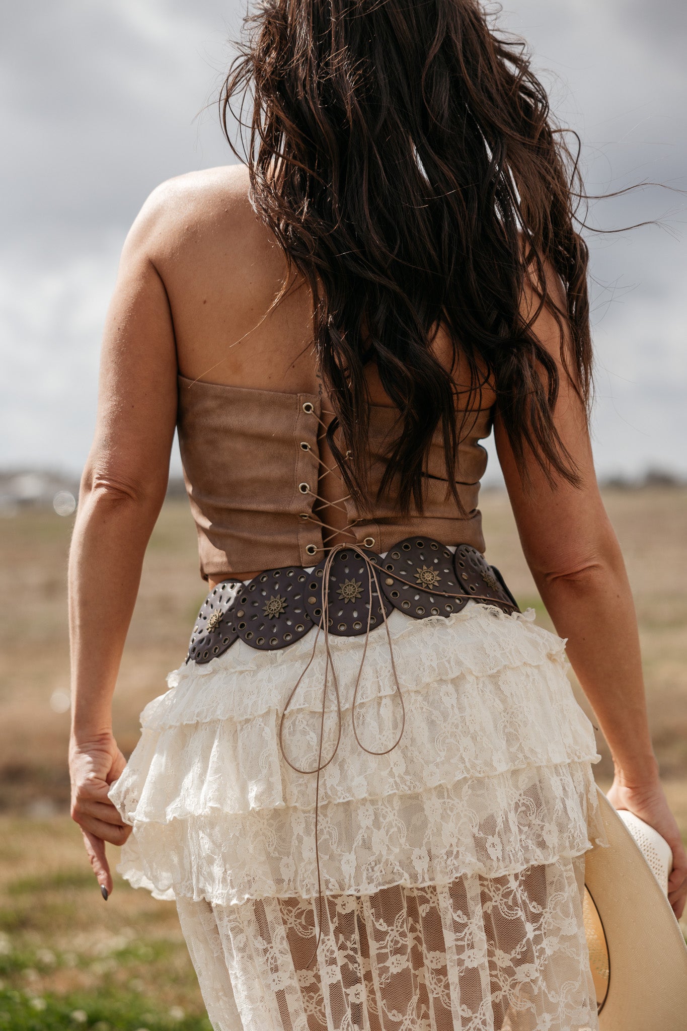 Woman in boho western lace skirt, leather corset top, and concho belt outdoors