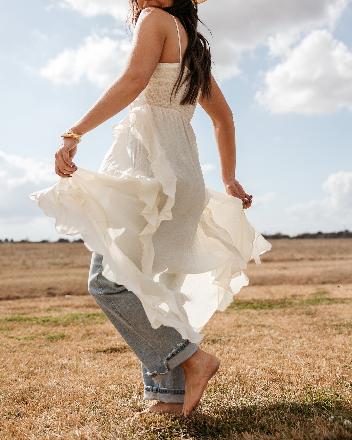 Woman in cowgirl hat, white western boho dress and jeans in a sunny outdoor field