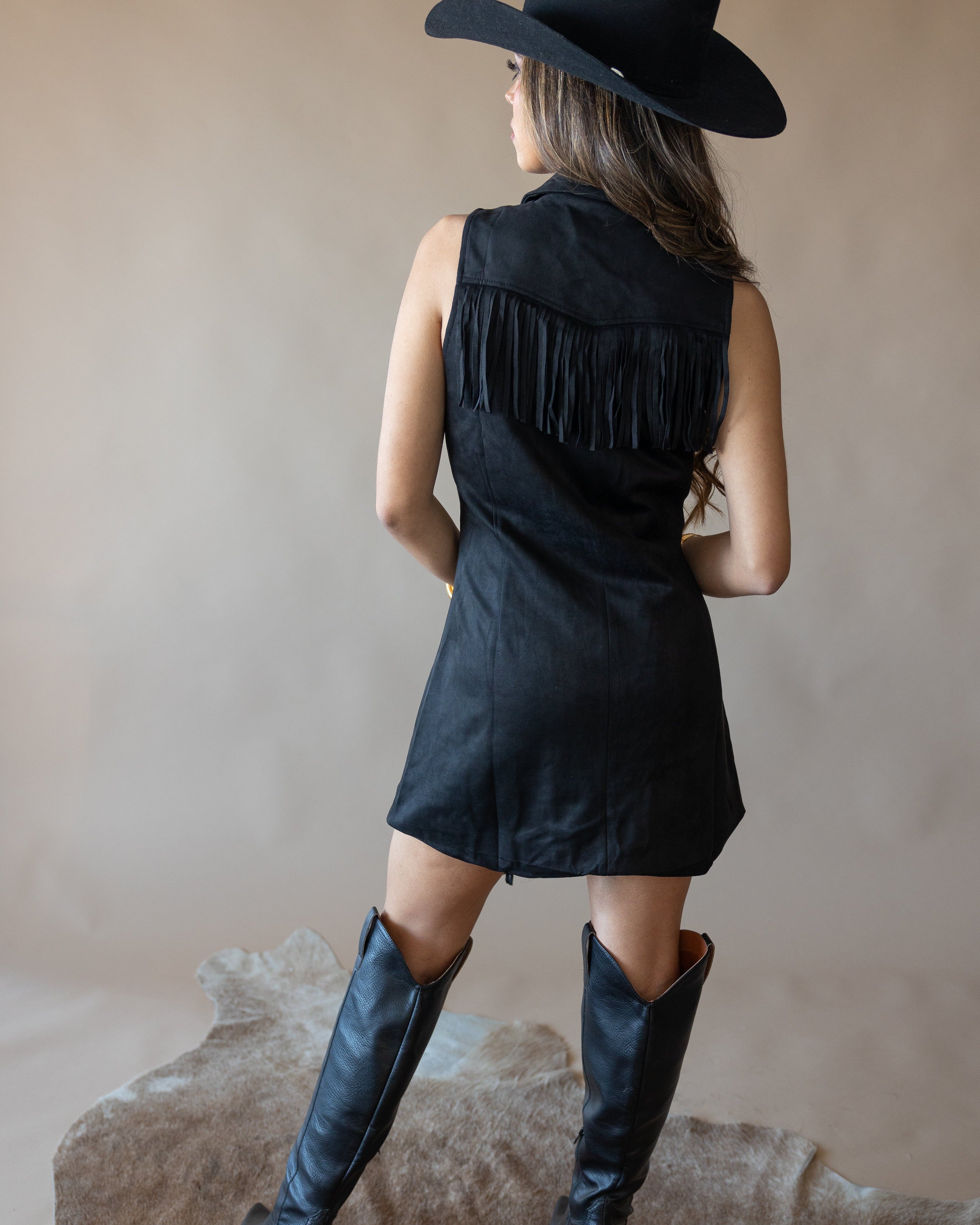 Woman in black fringe western dress, cowboy boots, and hat on cowhide rug, western boho style