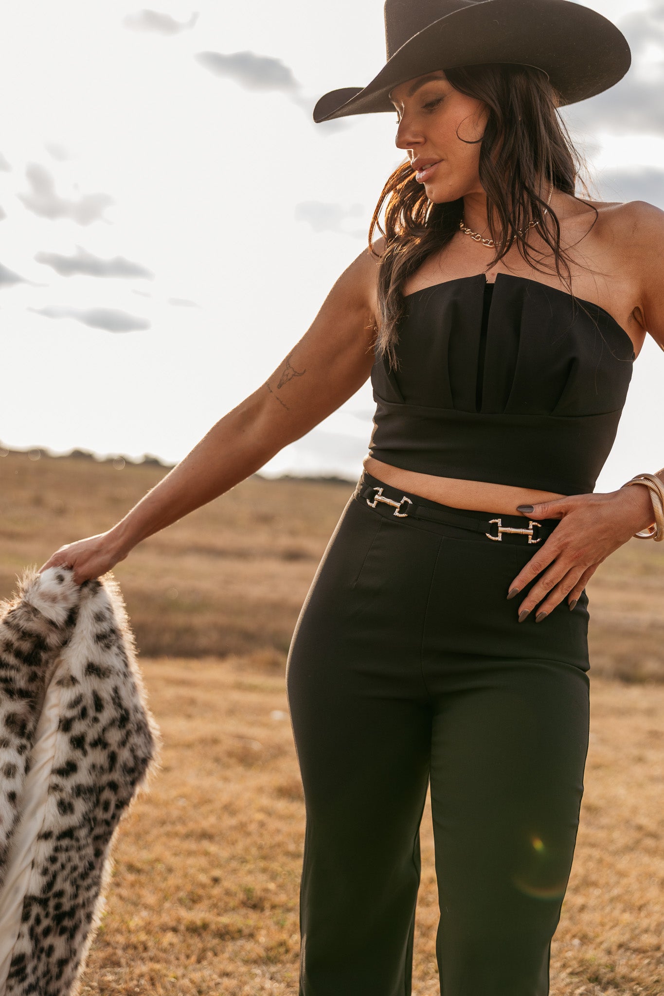 Woman in western black strapless top, high-waisted pants, and cowboy hat outdoors