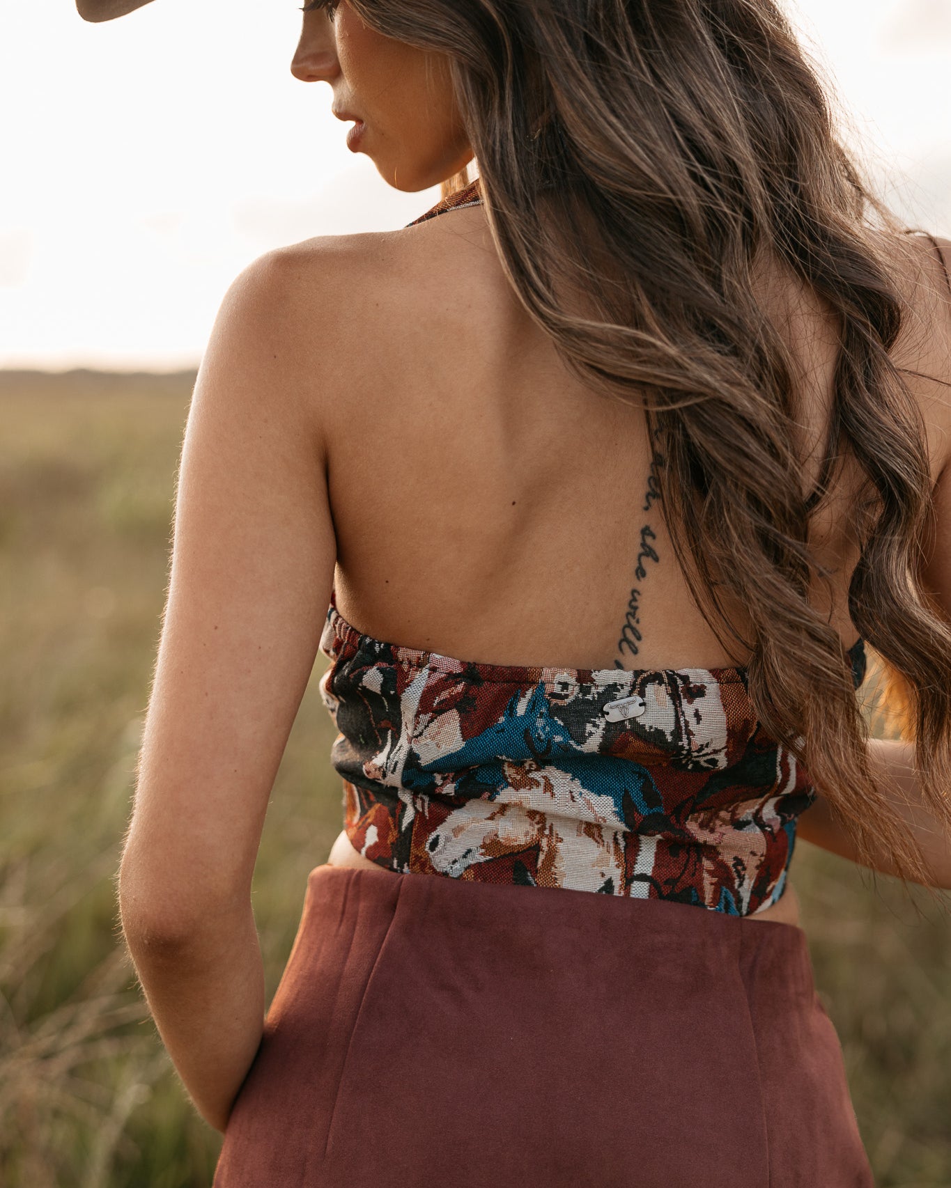 women wearing horse pattern halter top with low back and a Burgundy skirt standing in a field.