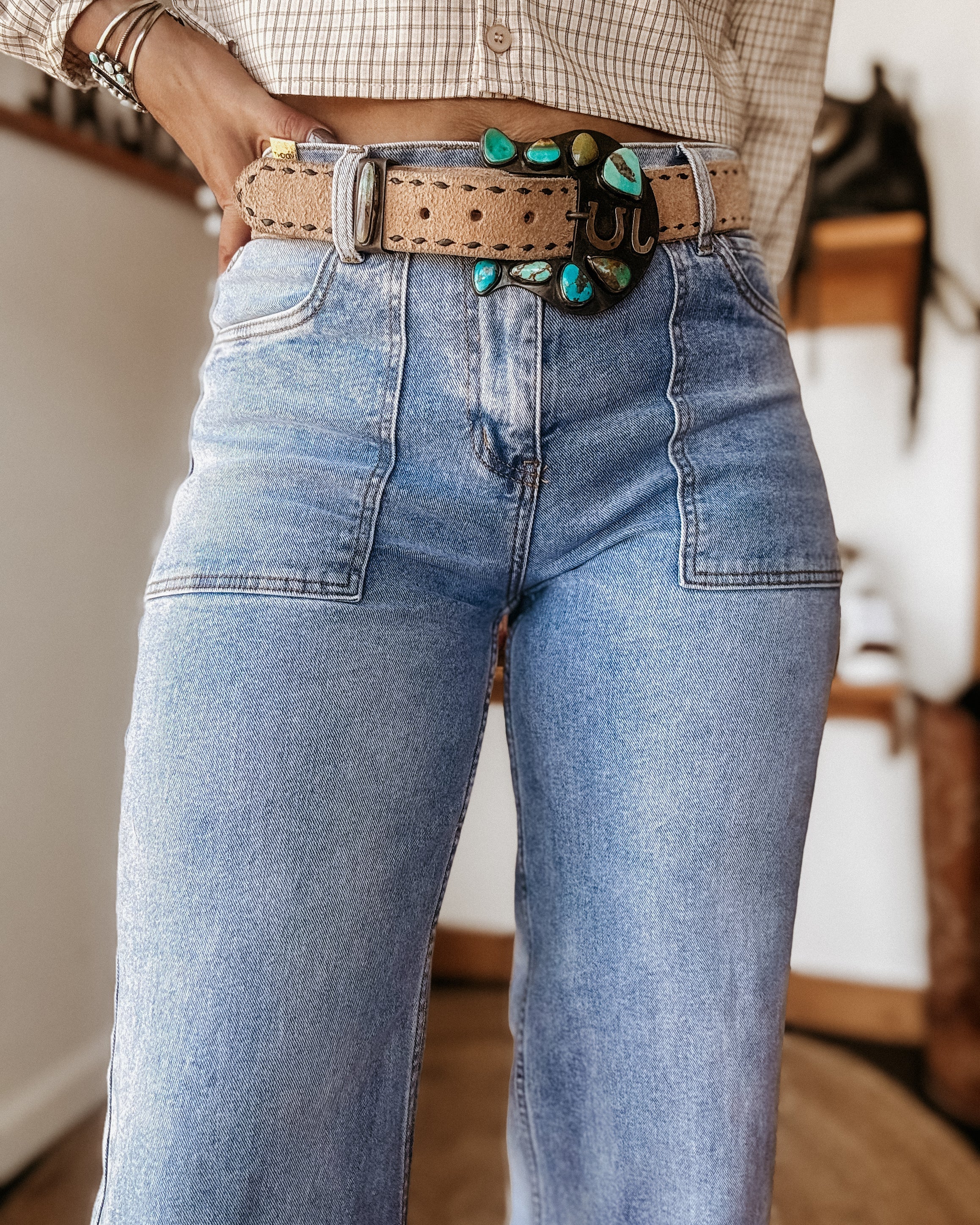 Woman wearing high-waisted flare jeans, a boho turquoise belt, and a plaid blouse.