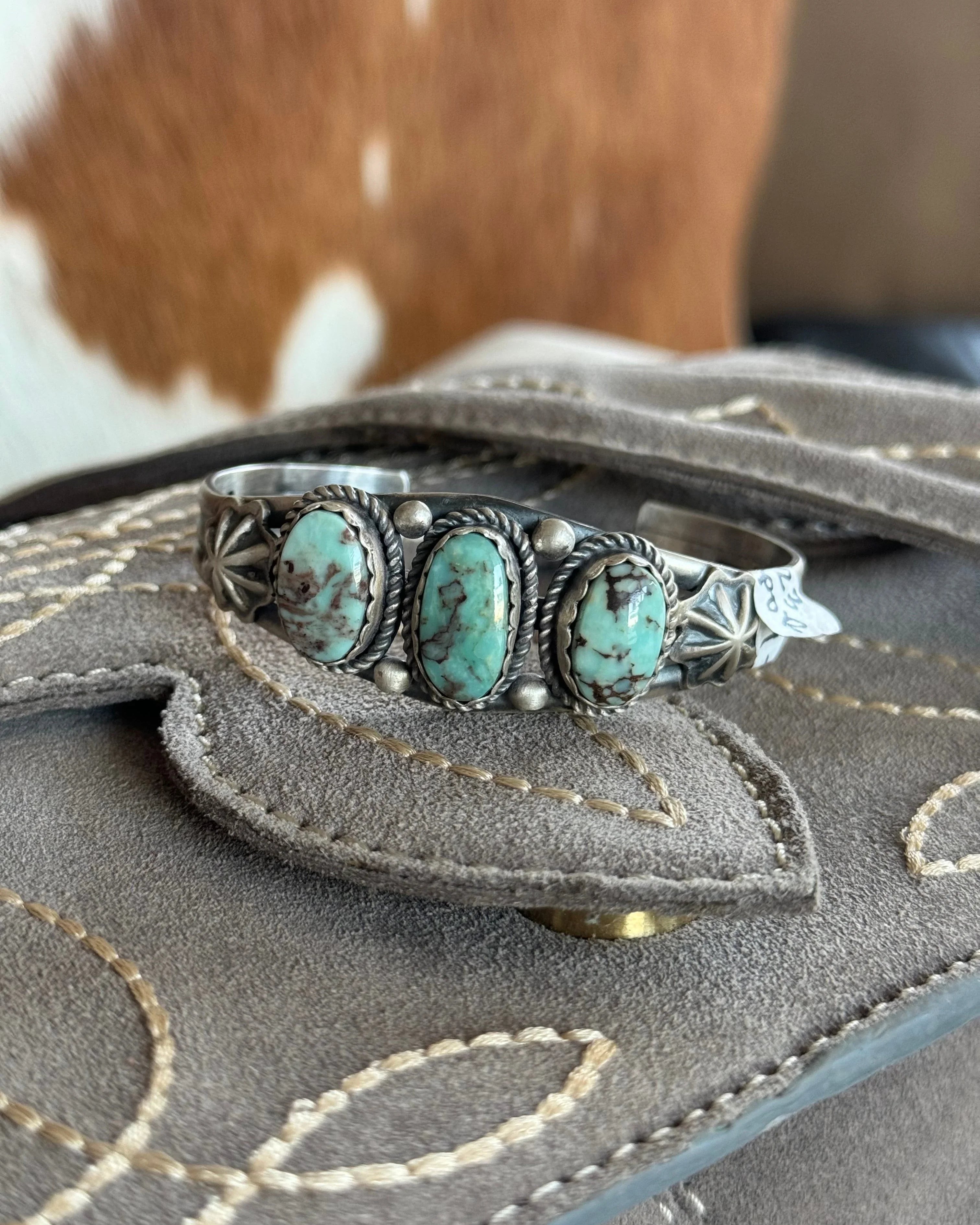 Western turquoise silver cuff bracelet with three stones on suede cowboy boot, cowhide background
