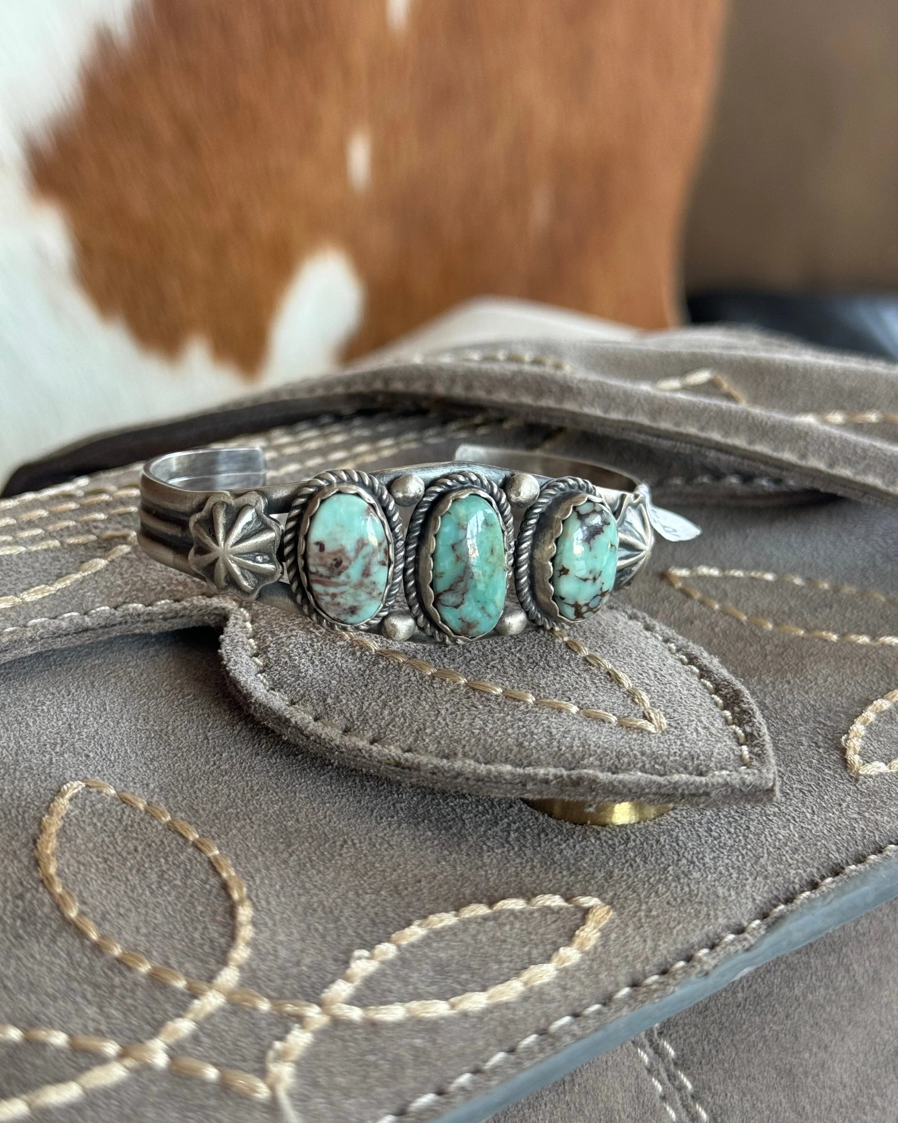 Turquoise western boho cuff bracelet on embroidered suede clutch with cowhide background
