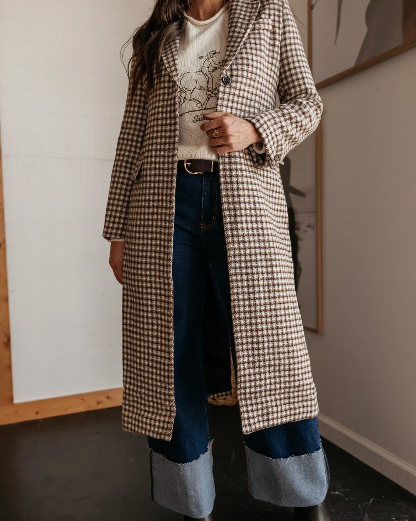 Woman in western boho plaid long coat, graphic sweater, two-tone jeans and cowboy hat
