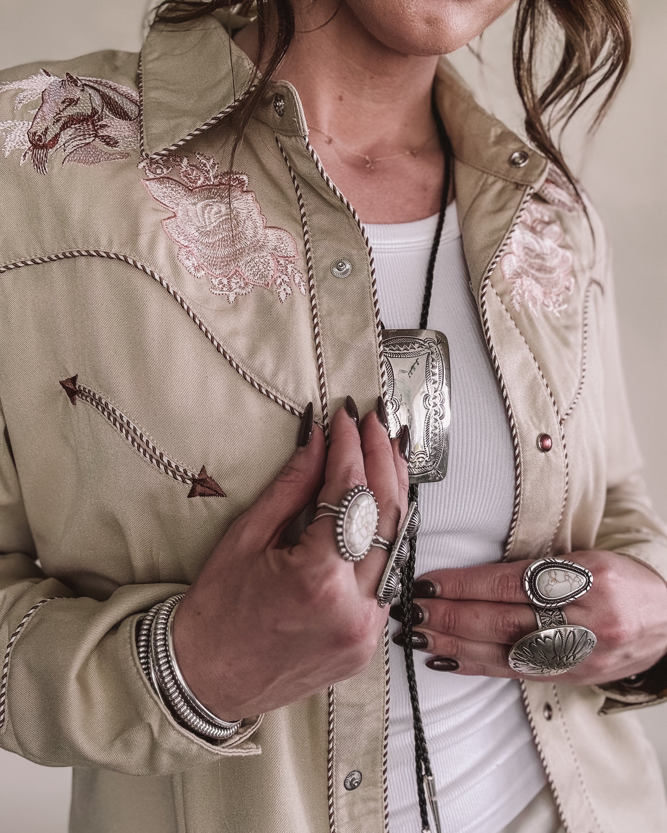 Woman wearing a western embroidered shirt with chunky silver rings and boho jewelry
