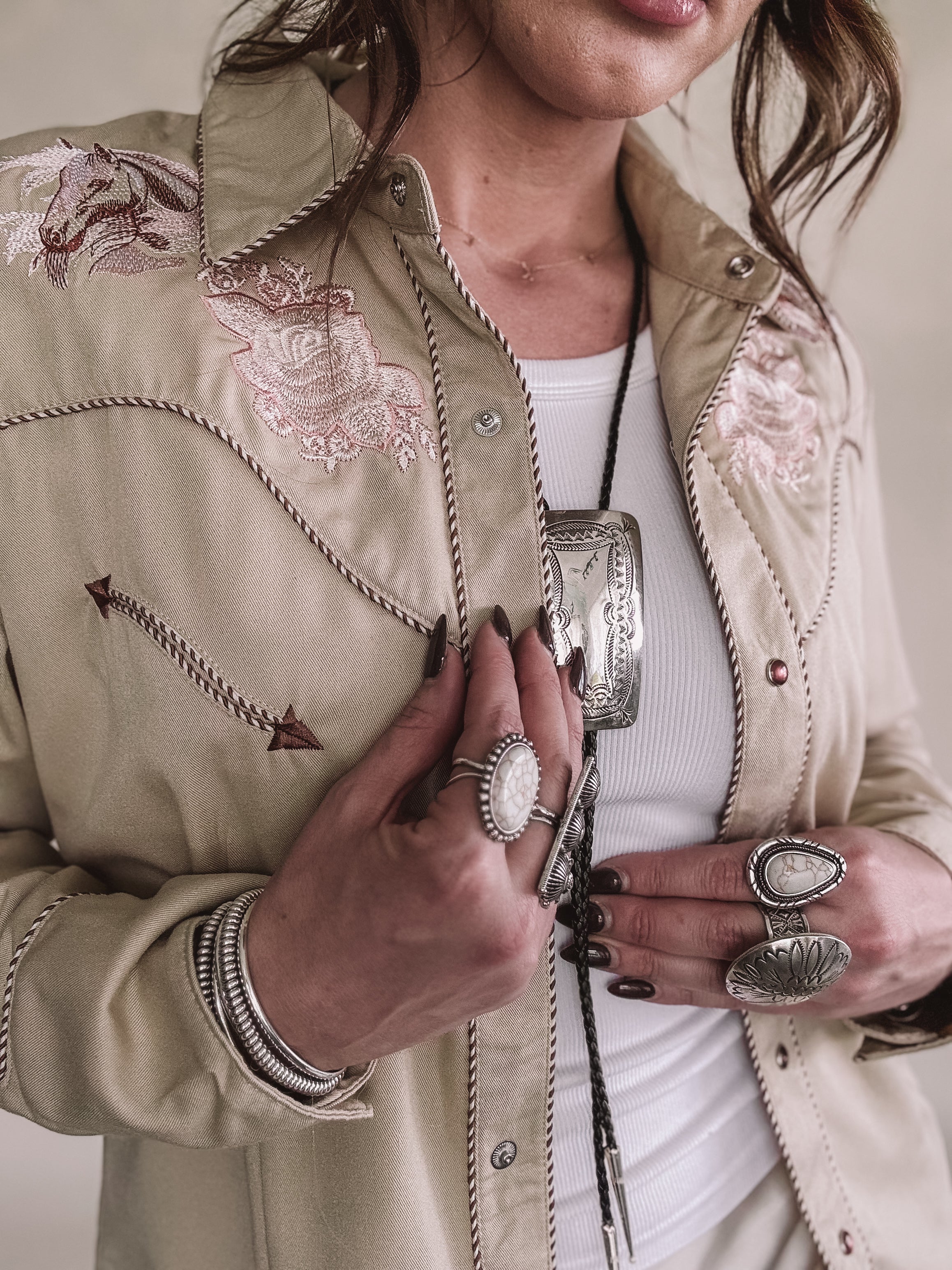 Woman wearing a western embroidered shirt with chunky silver rings and boho jewelry