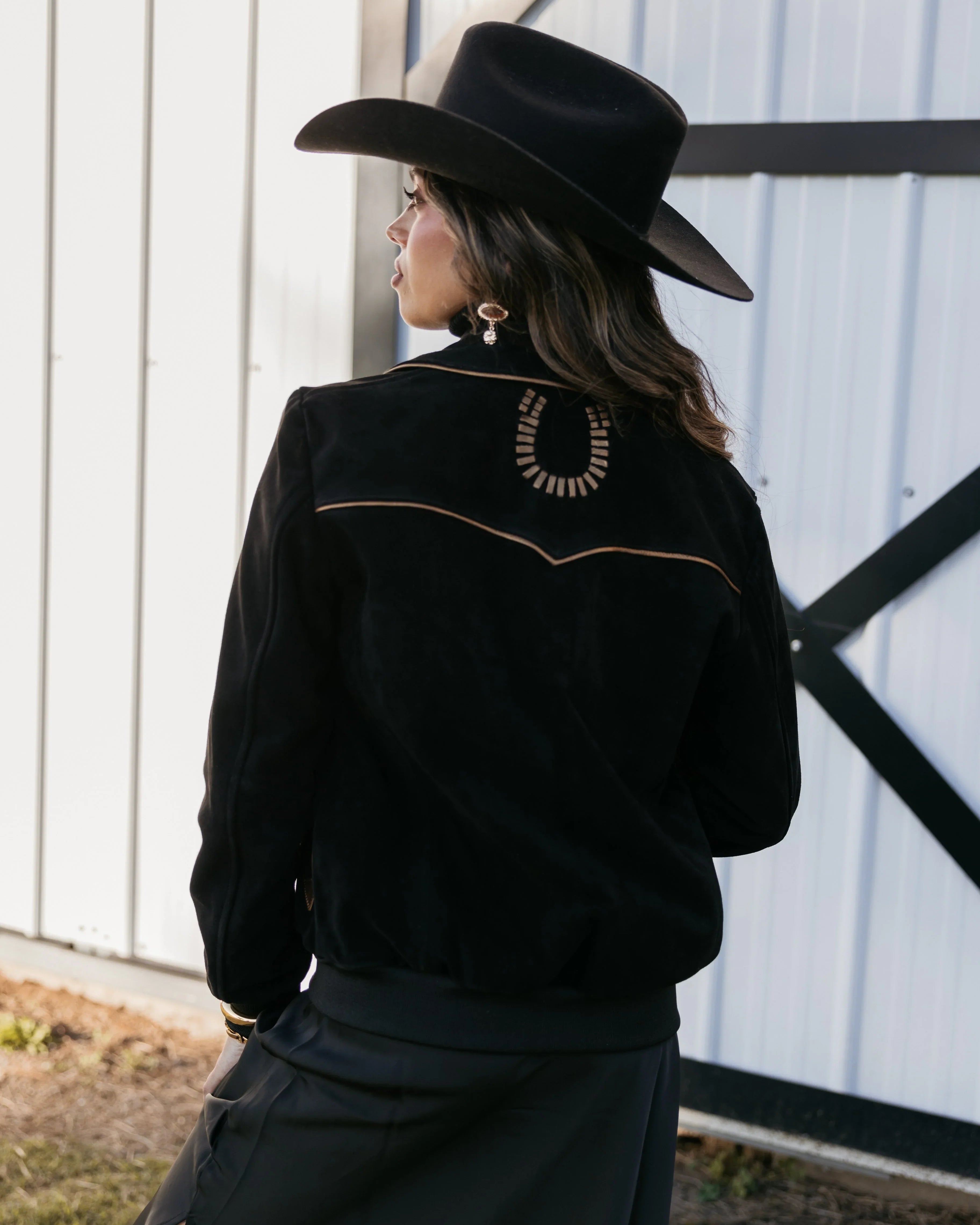 Woman in black western hat and jacket with horseshoe detail, boho cowgirl style outdoors