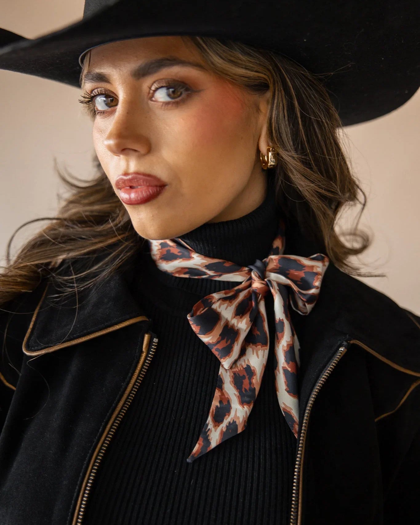 Woman in western hat, black jacket, and animal print neck scarf, cowgirl boho style
