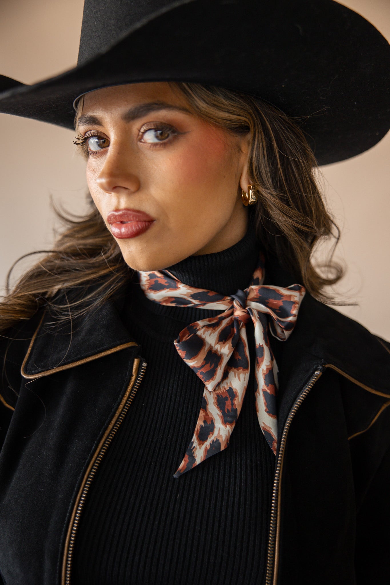 Woman in western hat, black jacket, and animal print neck scarf, cowgirl boho style
