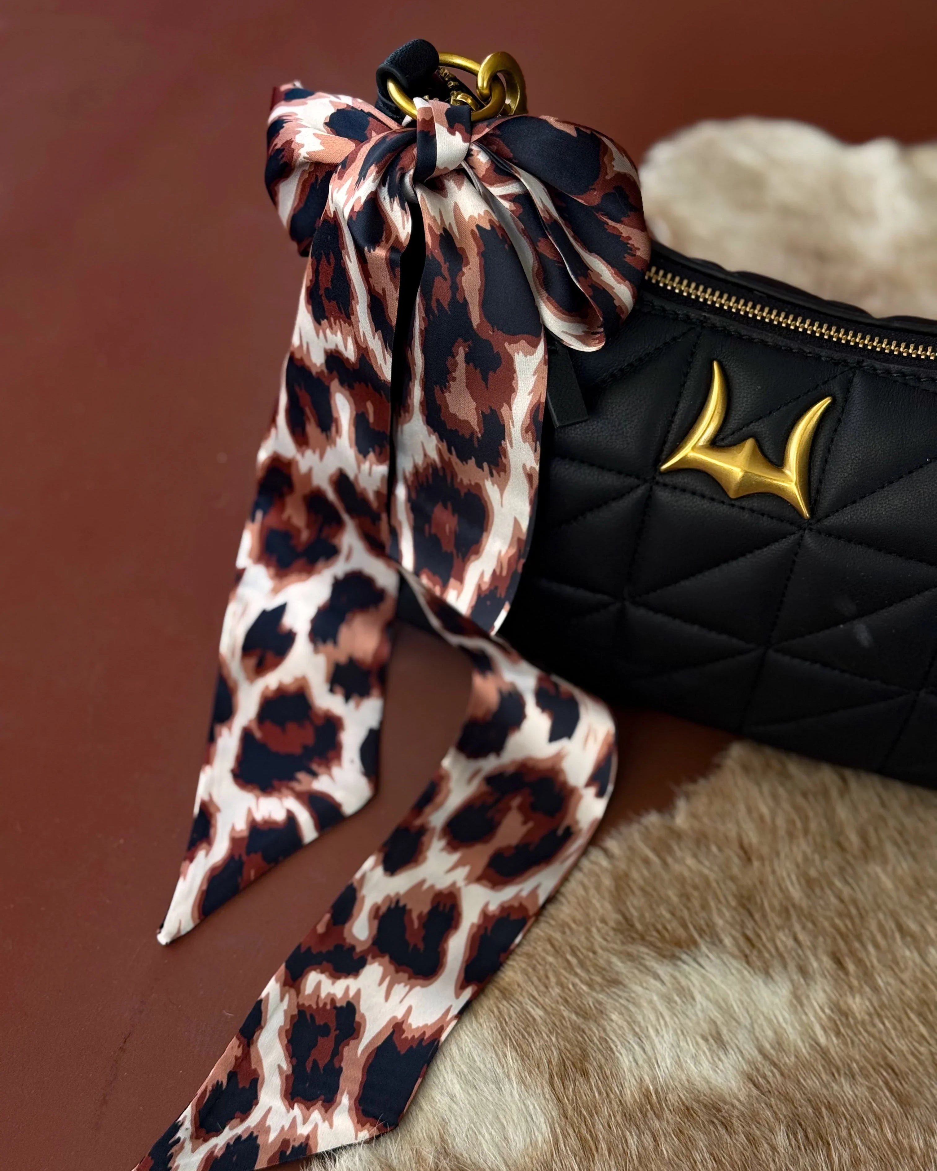 Quilted black western handbag with gold accent and leopard print bow on cowhide surface