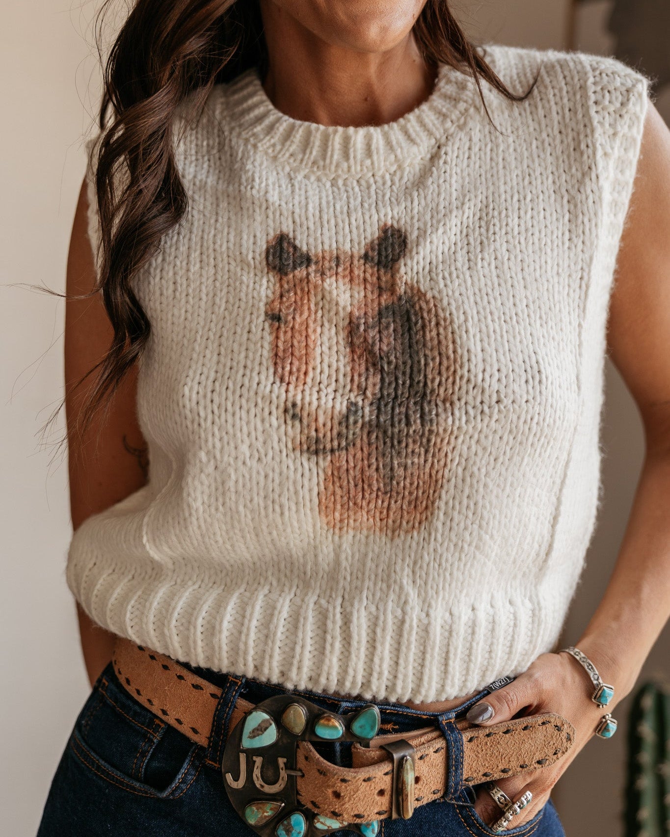 Woman in white knit horse sweater, western belt with turquoise, and boho jewelry