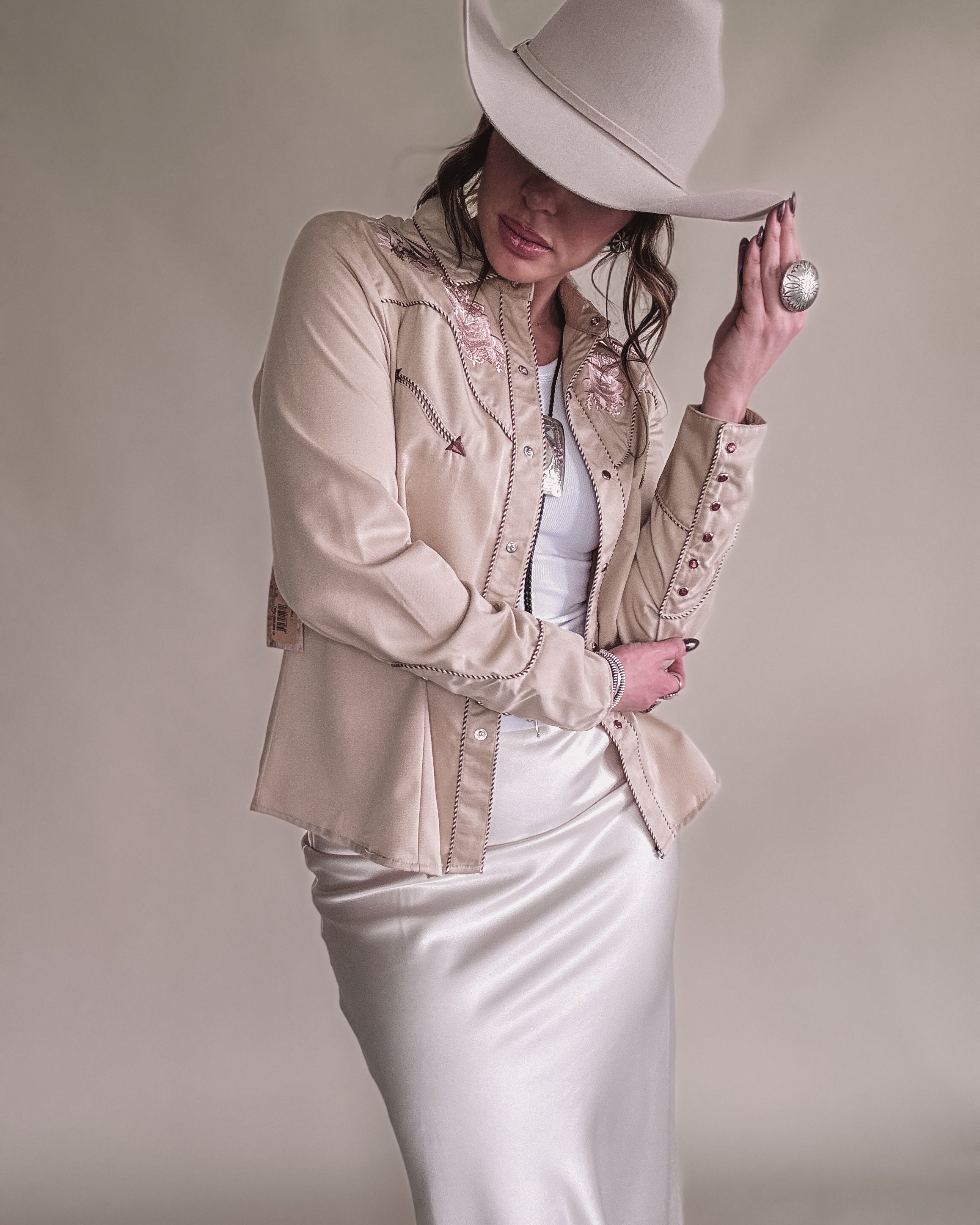 Woman in beige embroidered western shirt, satin skirt, and cowboy hat, showcasing boho cowgirl style.