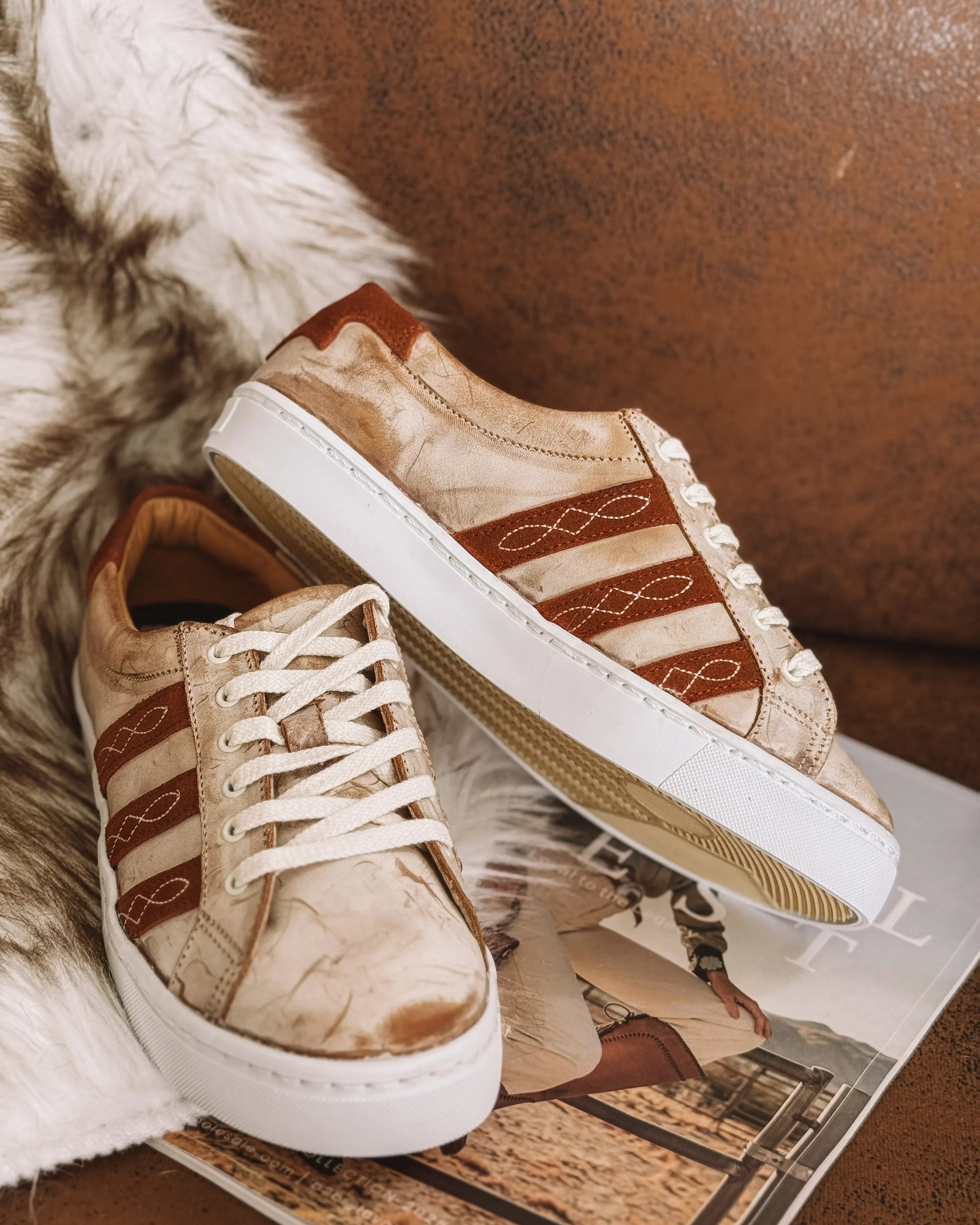 Tan and brown western sneakers with embroidered details on a faux fur rug and magazine.