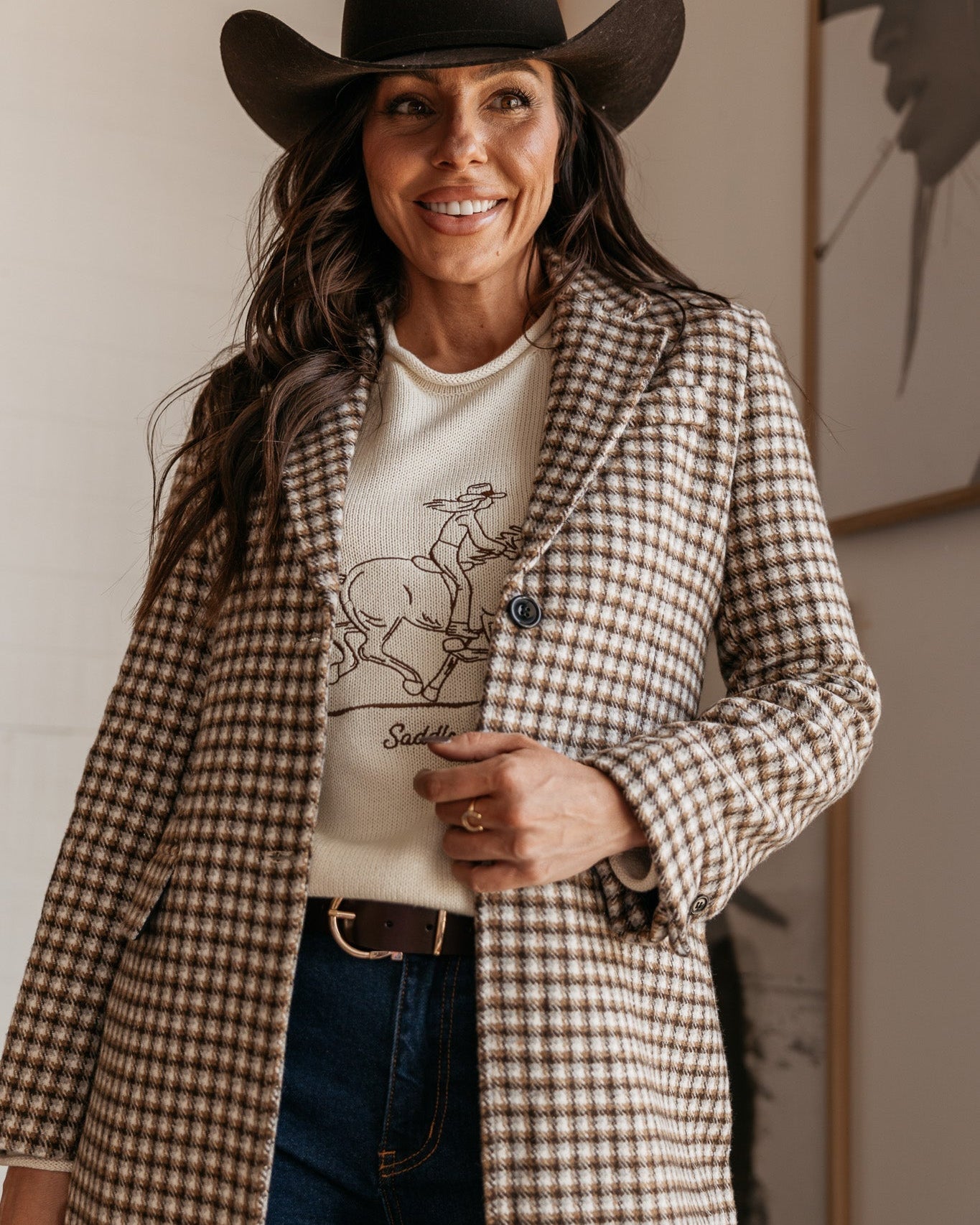 Woman in western boho outfit with plaid coat, cowboy hat, and graphic rodeo sweater