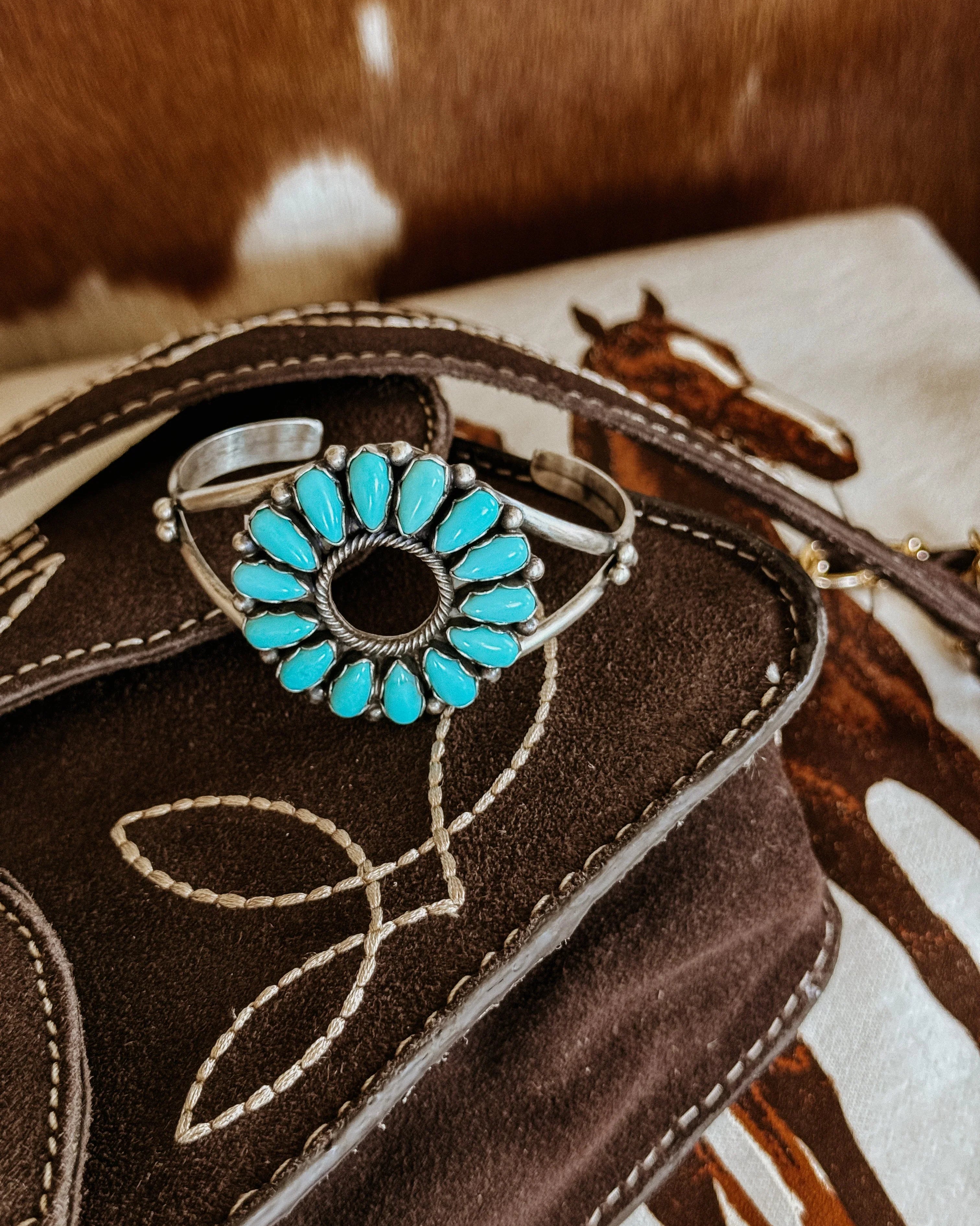 Turquoise stone western cuff bracelet on embroidered suede bag, horse print background.
