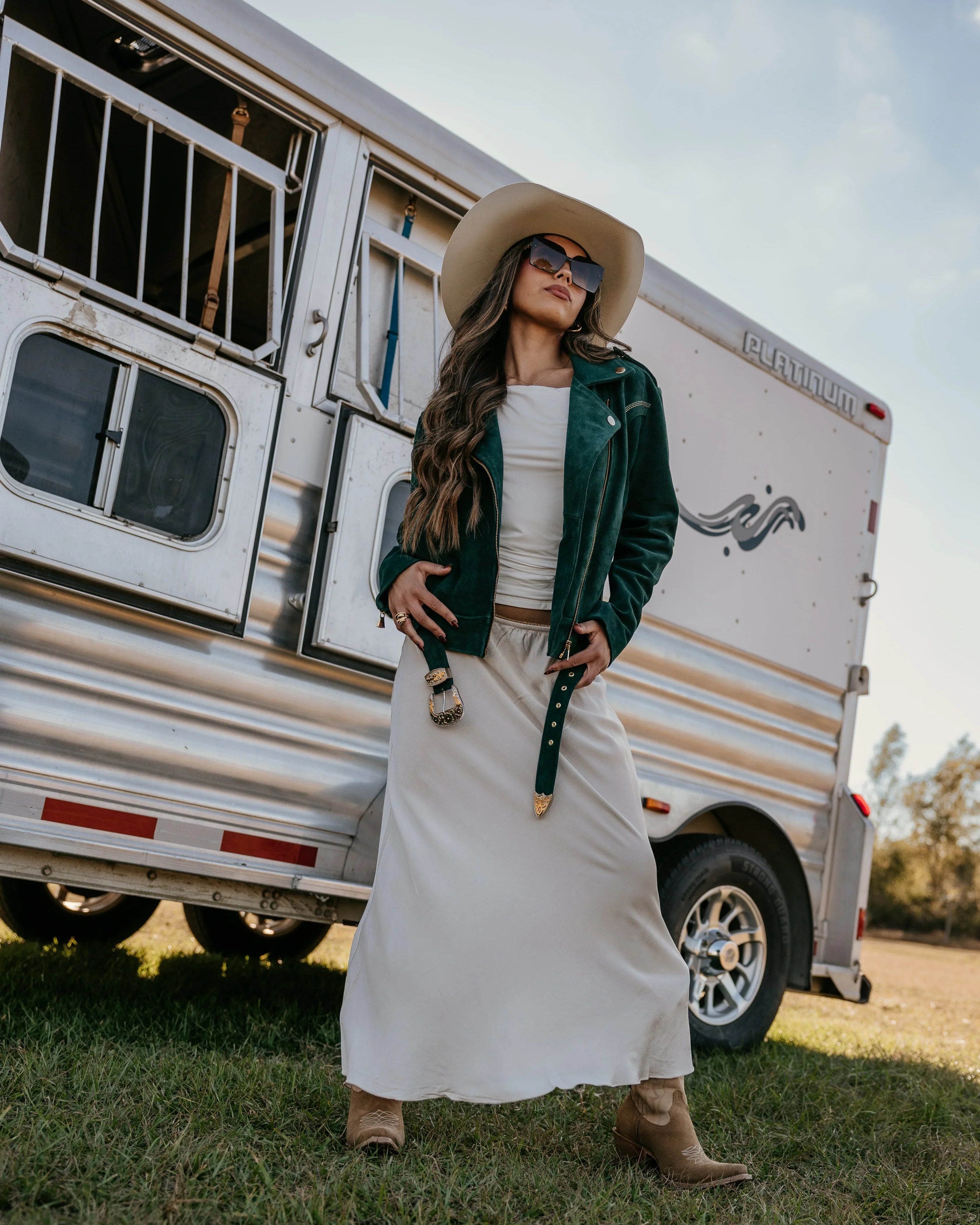 Woman in western boho outfit with suede jacket, maxi skirt, cowboy hat and boots by horse trailer