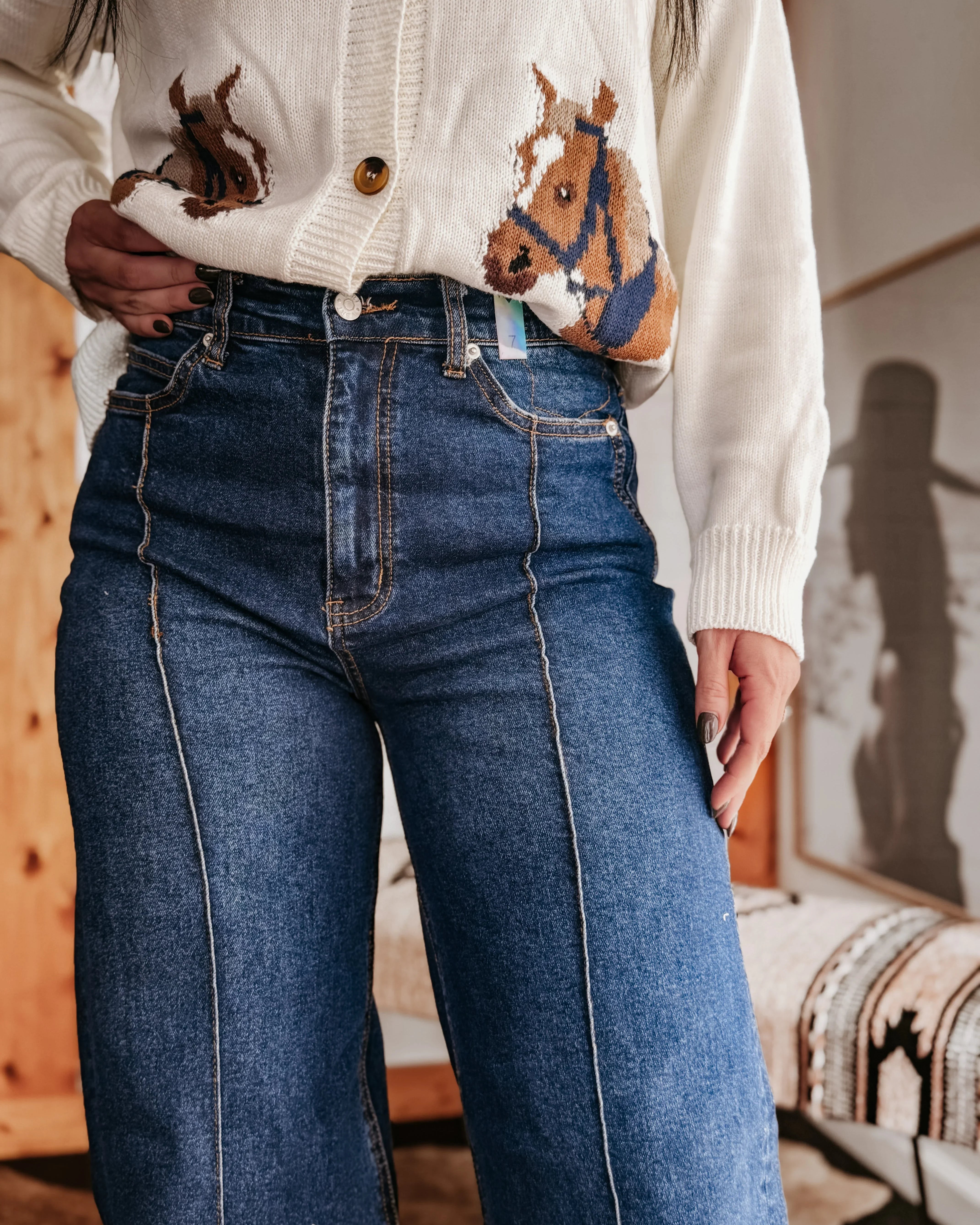 Woman wearing high-waisted wide leg jeans and a white sweater with horse design, western style