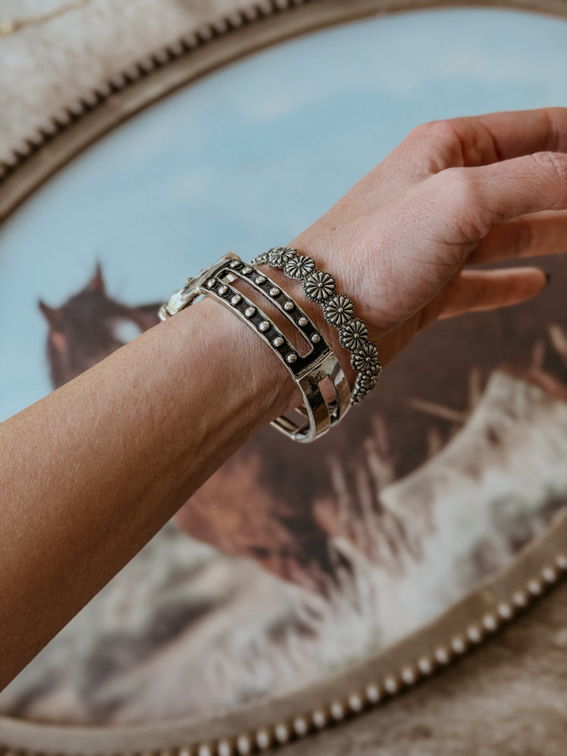 Woman wearing western silver cuff and floral concho bracelets with a horse art background
