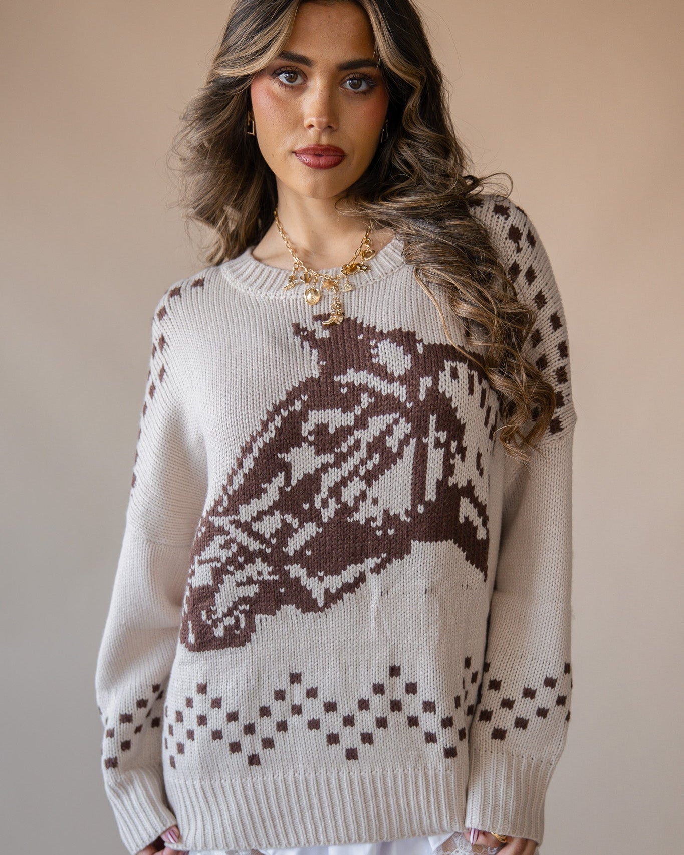 Woman wearing beige western sweater with brown horse pattern, lace skirt, and gold necklace