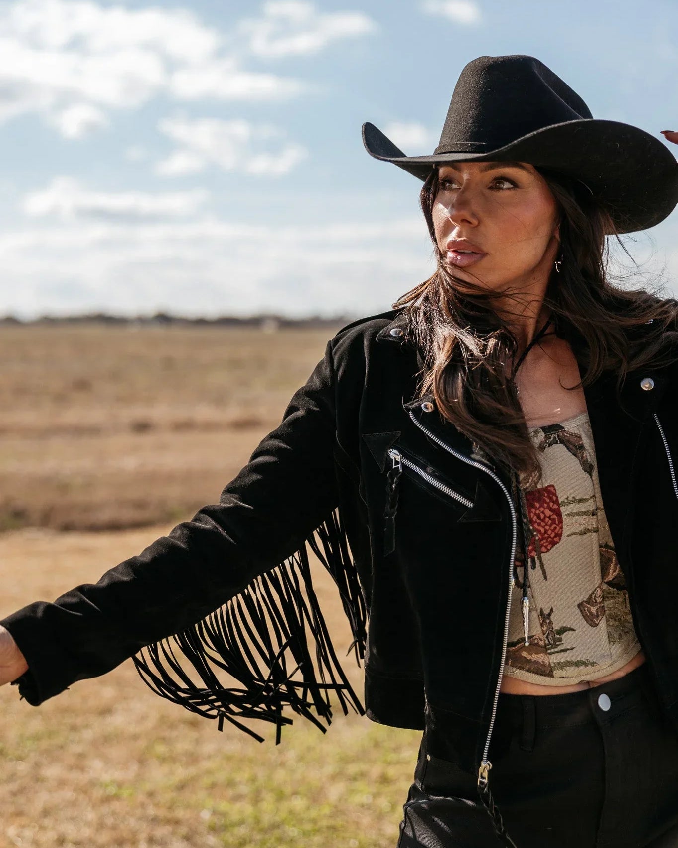 Woman in black fringe western jacket and cowboy hat outdoors, western boho outfit style