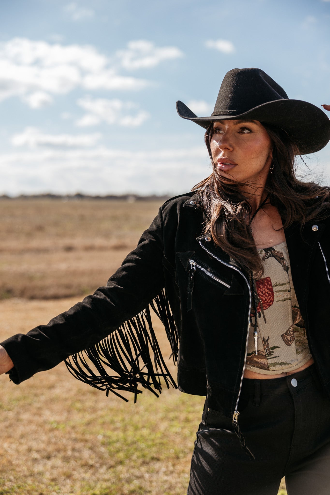 Woman in black fringe western jacket and cowboy hat outdoors, western boho outfit style