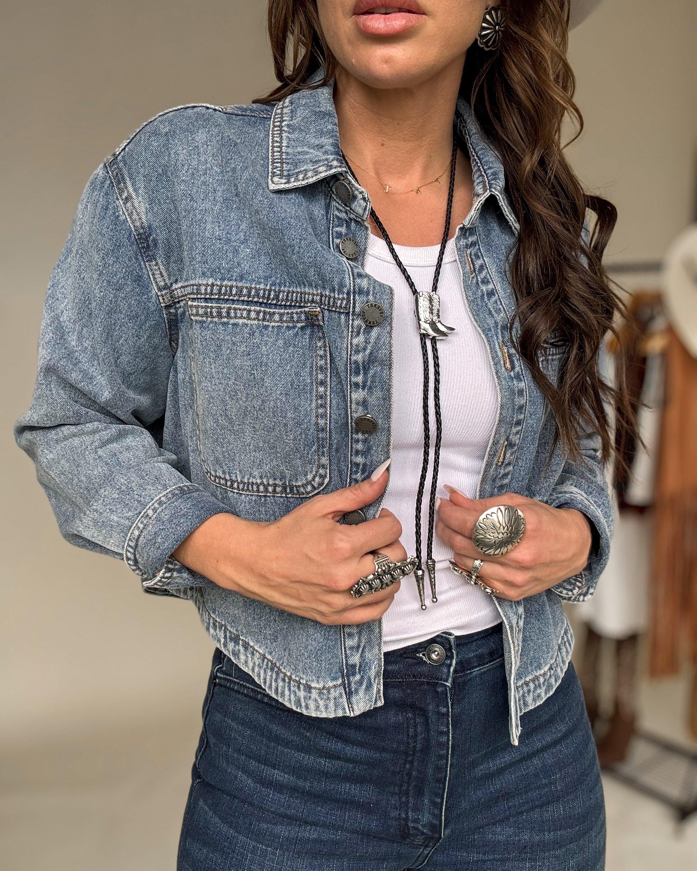 Woman in western boho outfit with denim jacket, white tank top, bolo tie, and silver jewelry