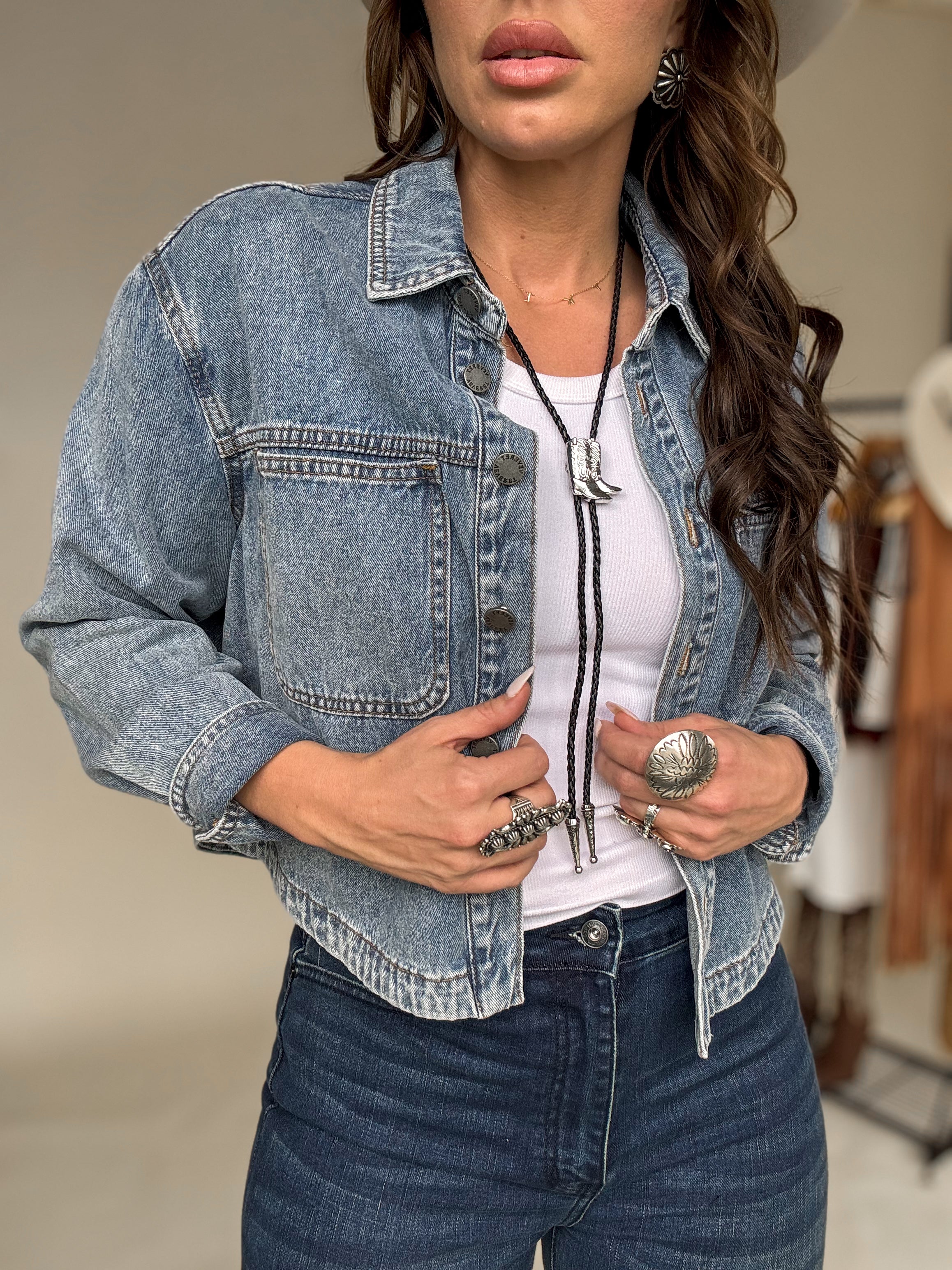 Woman in western boho outfit with denim jacket, white tank top, bolo tie, and silver jewelry