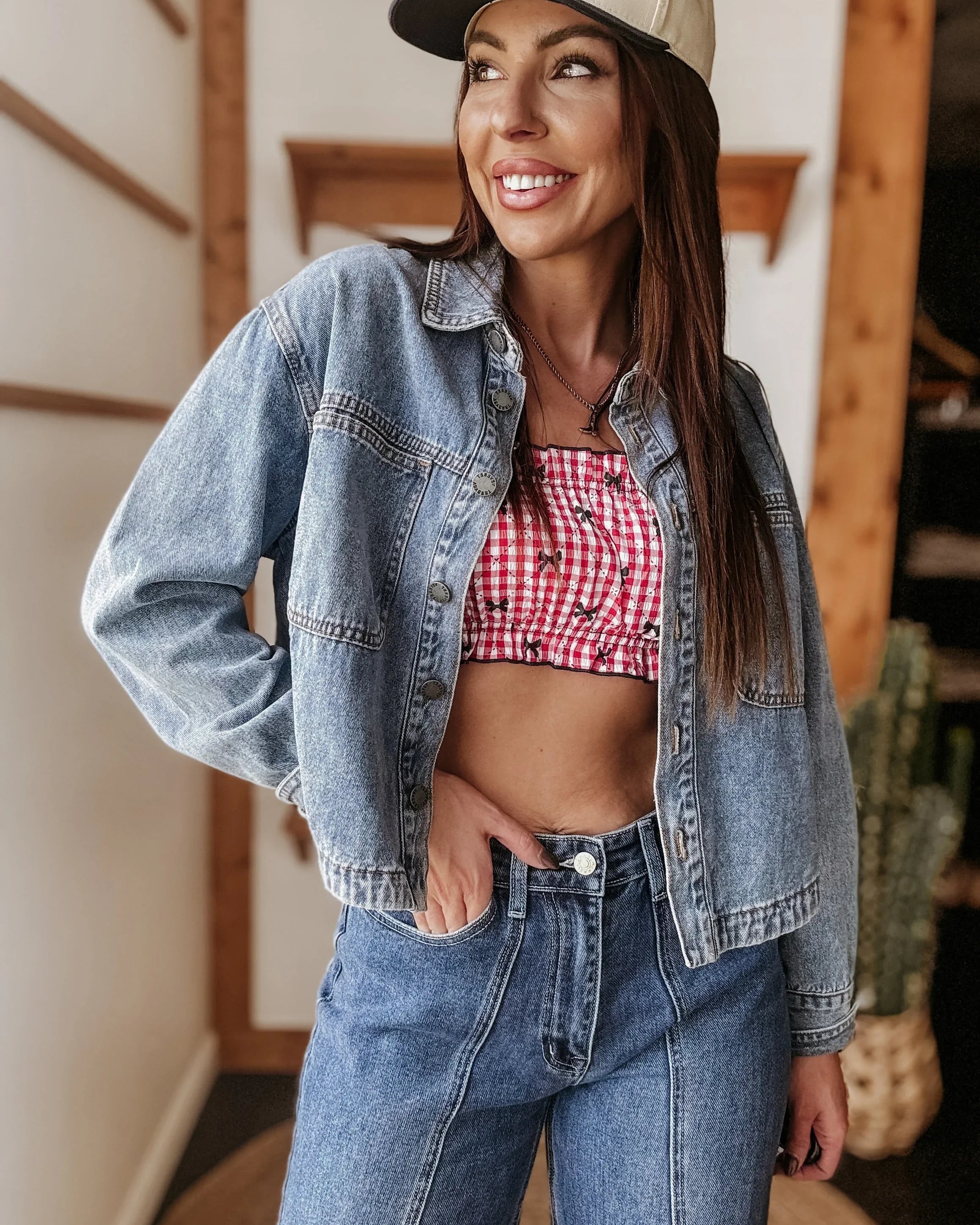 Woman in denim jacket and jeans, red gingham crop top, western hat, western boho style