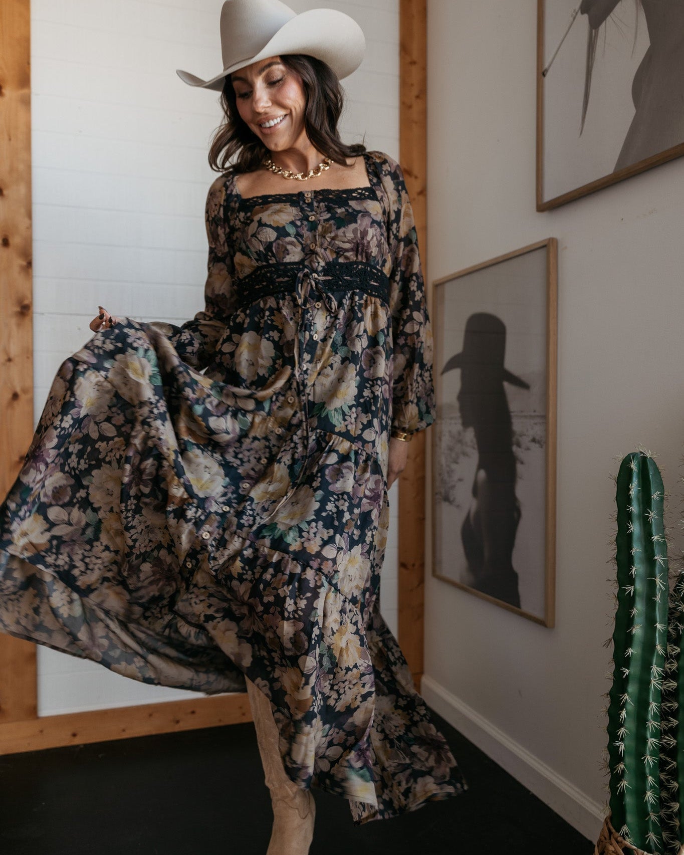 Woman in a white cowboy hat, floral maxi dress, and boots, styled in a western boho outfit indoors.