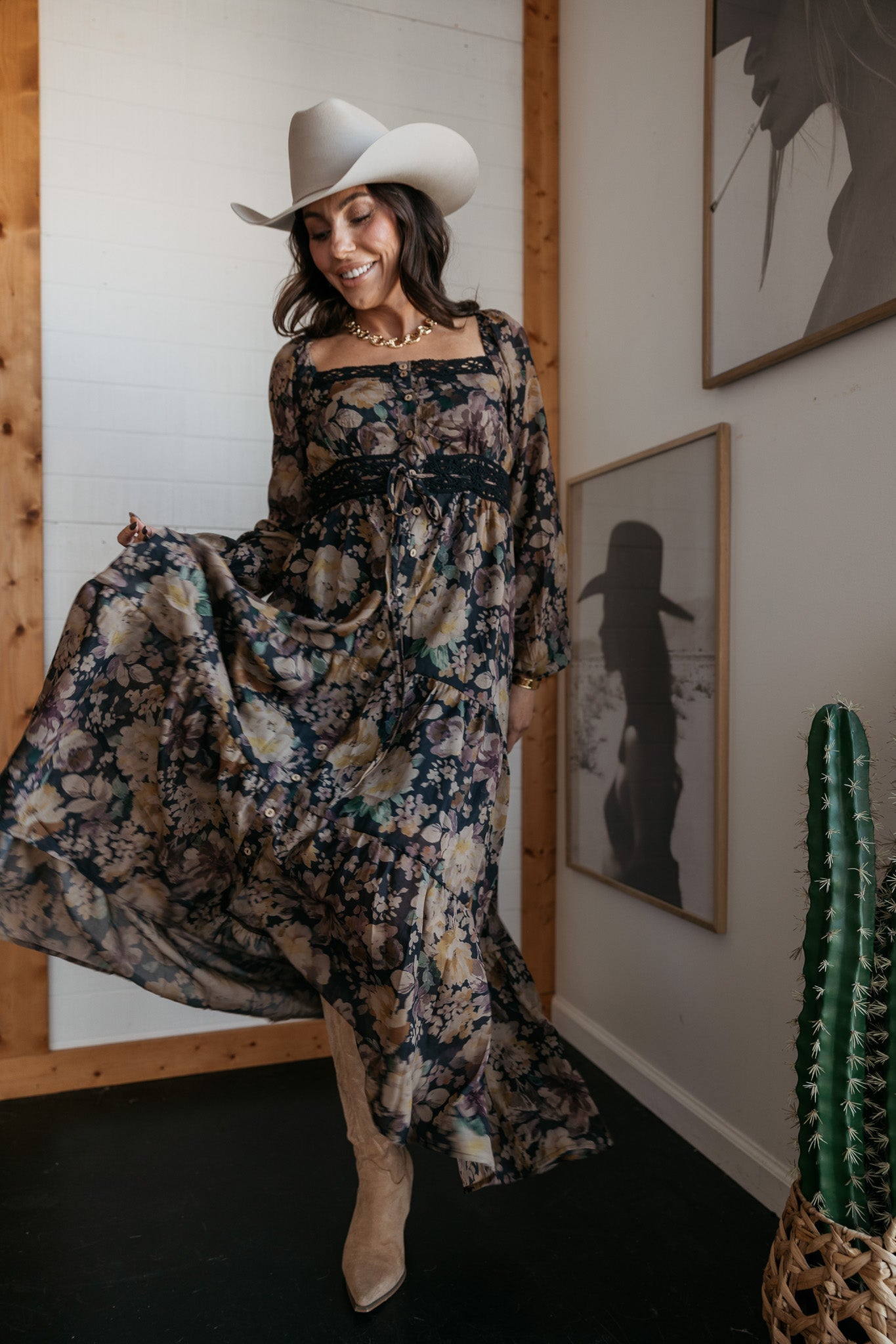 Woman in a white cowboy hat, floral maxi dress, and boots, styled in a western boho outfit indoors.