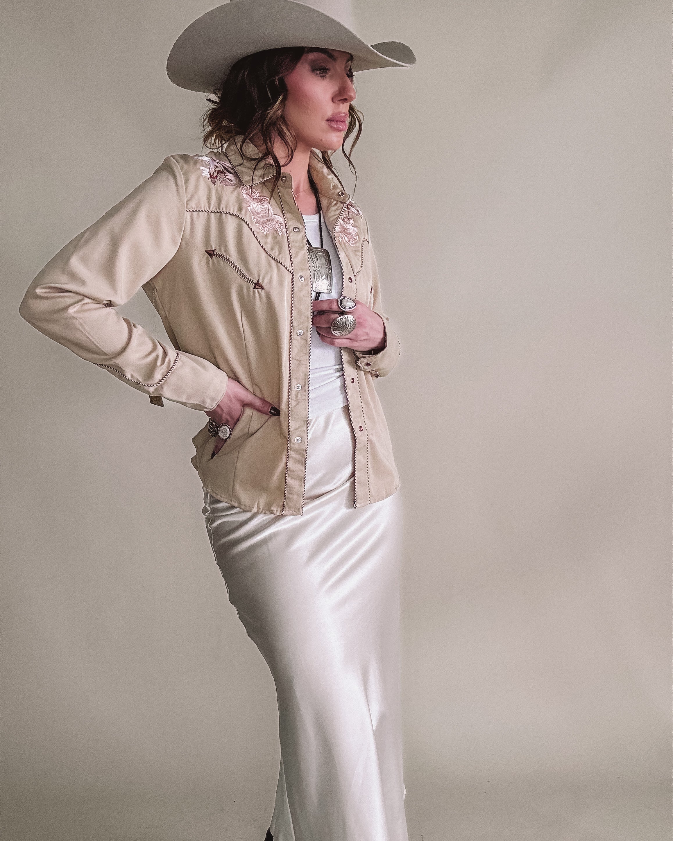 Woman in western boho outfit with cowboy hat, embroidered jacket, and satin skirt