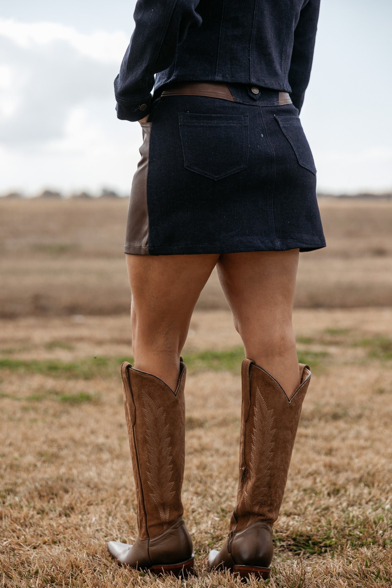 Woman wearing denim mini skirt and brown western cowboy boots outdoors