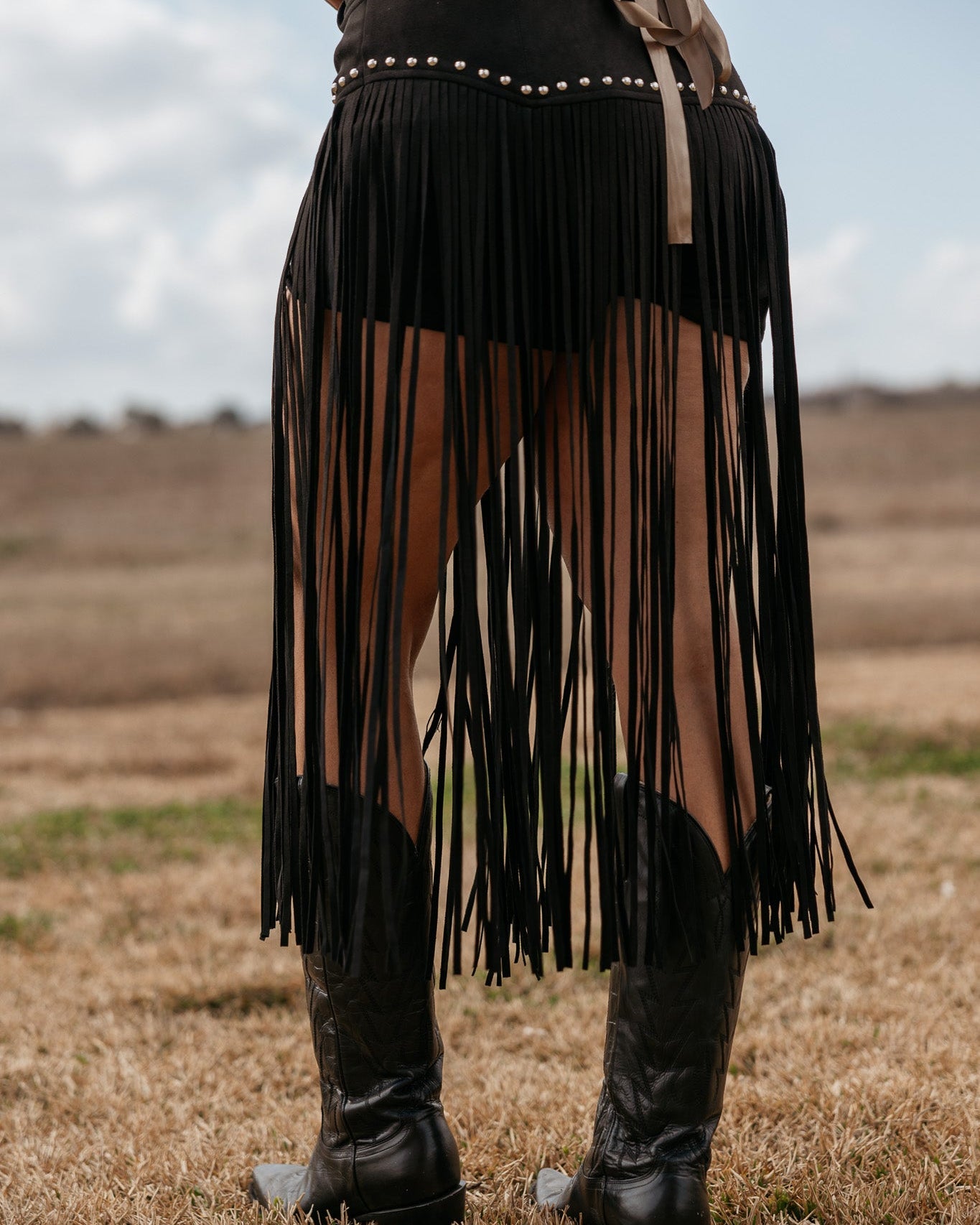 Woman wearing black fringe skirt with studs and cowboy boots in western outdoor setting
