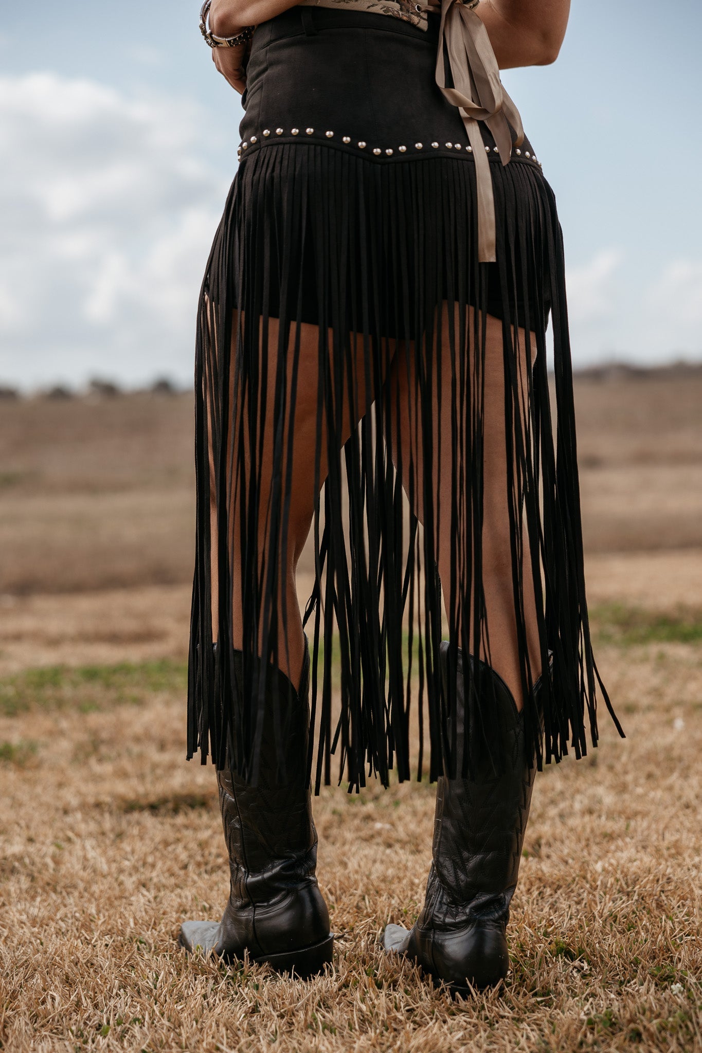 Woman wearing black fringe skirt with studs and cowboy boots in western outdoor setting