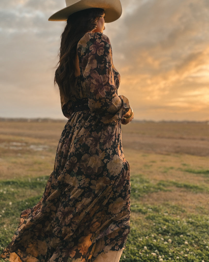 Woman in a floral western boho dress and cowboy hat outdoors at sunset