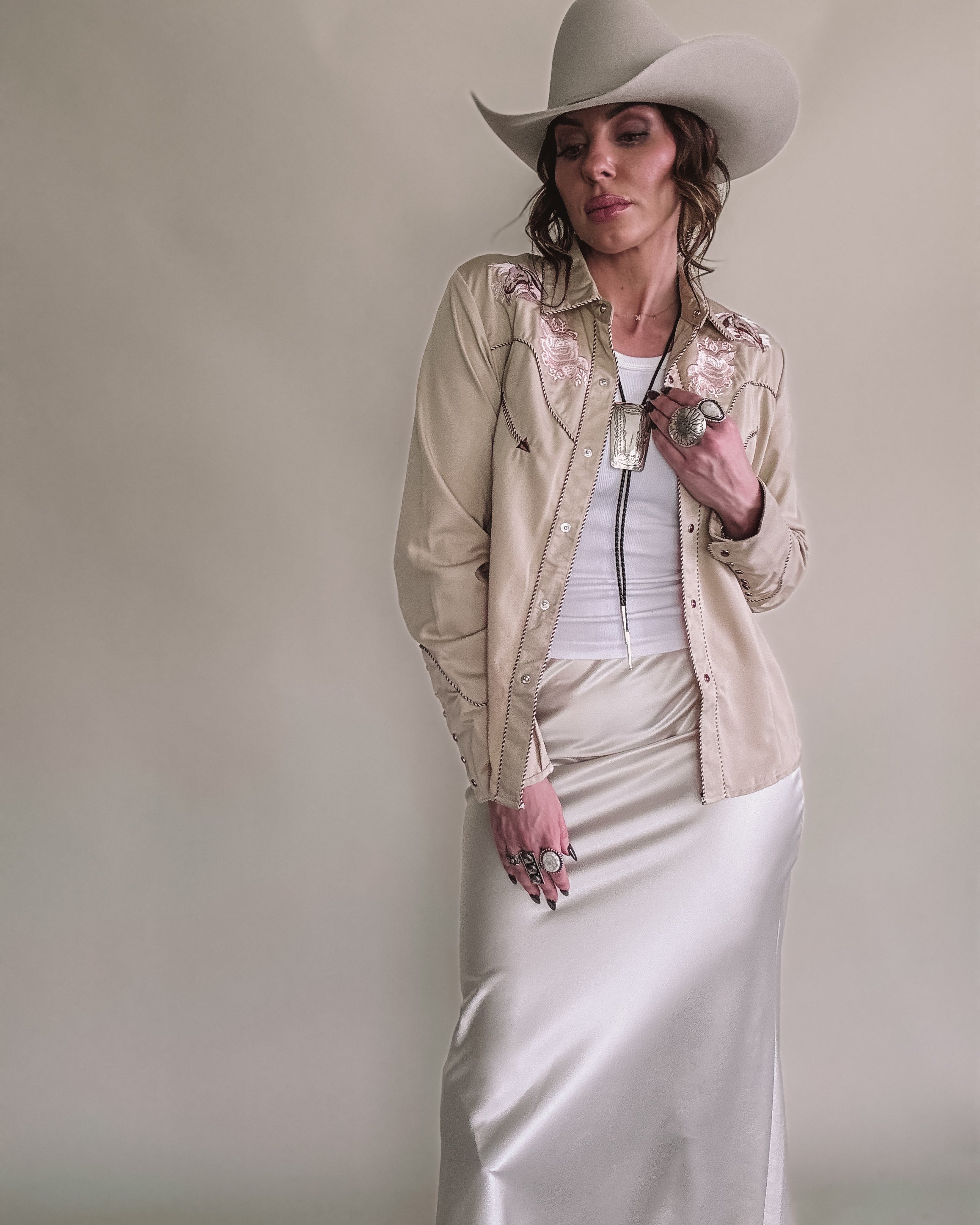 Woman in western boho outfit with cream cowboy hat, embroidered shirt, and satin skirt