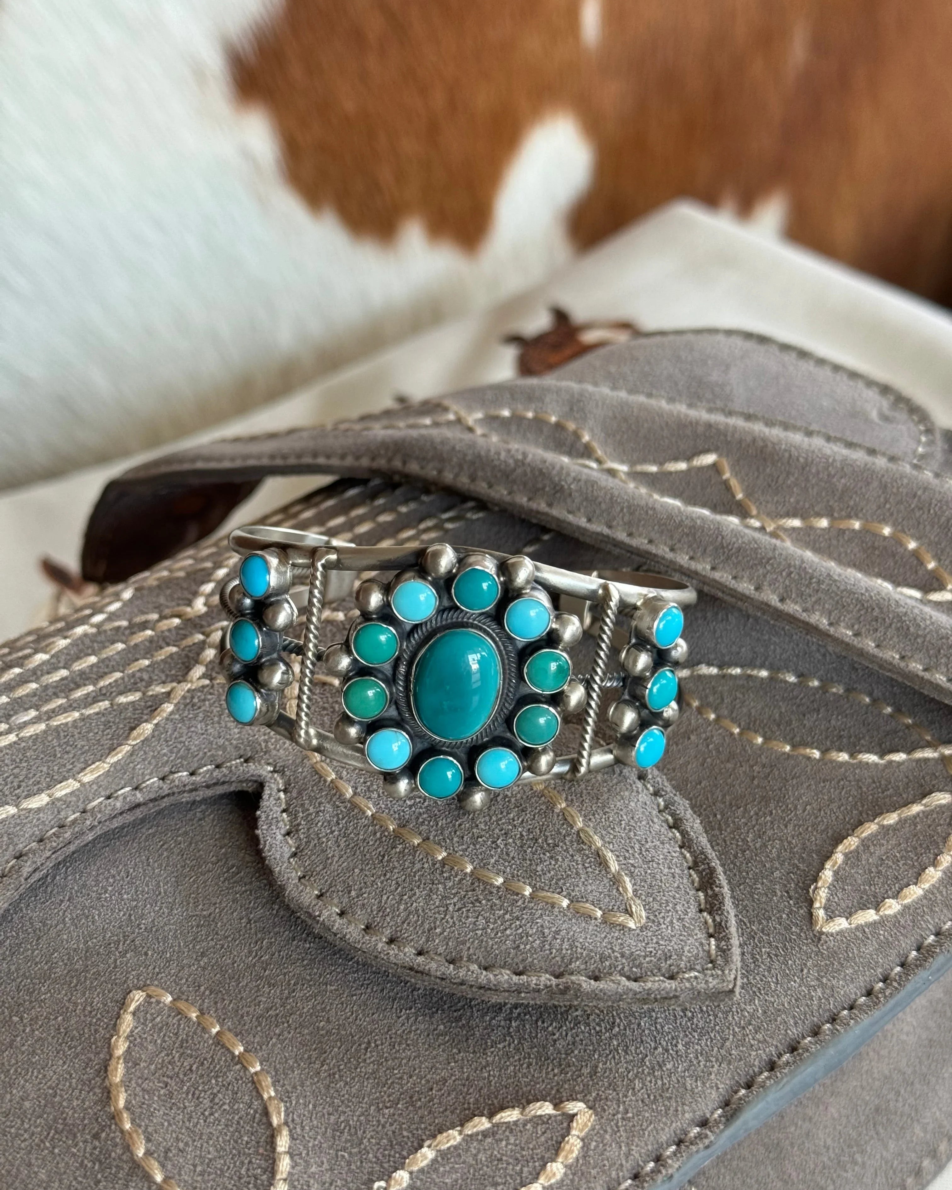 Turquoise and silver western cuff bracelet on embroidered grey suede purse, cowhide background