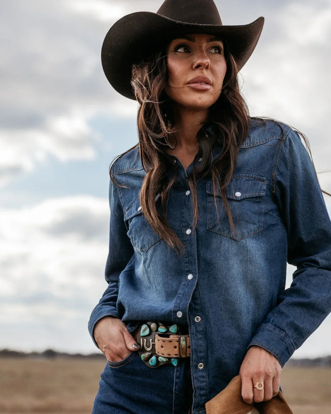 Woman in cowgirl hat and denim shirt with turquoise western belt outdoors