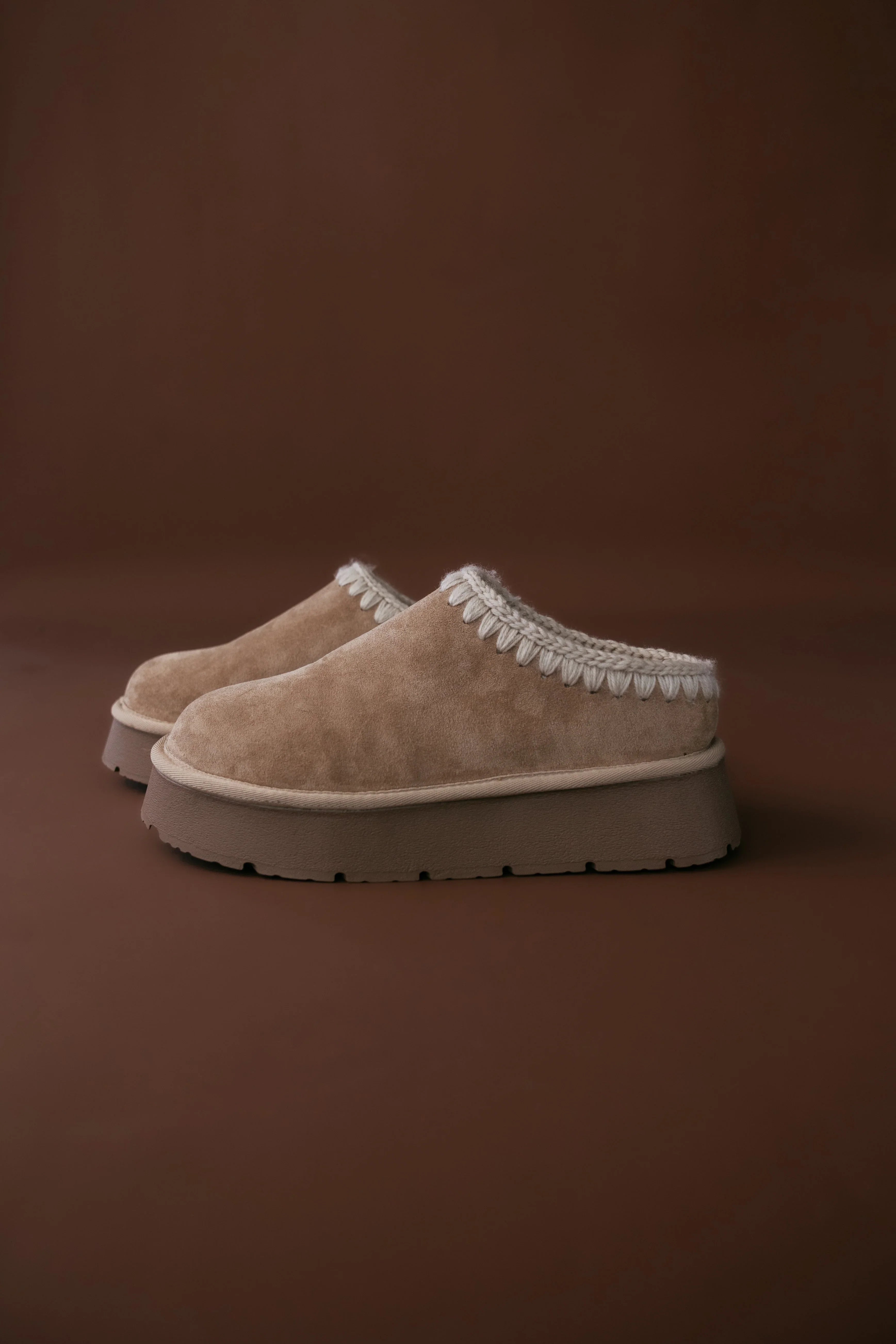 Pair of beige slippers with white trim on a brown background